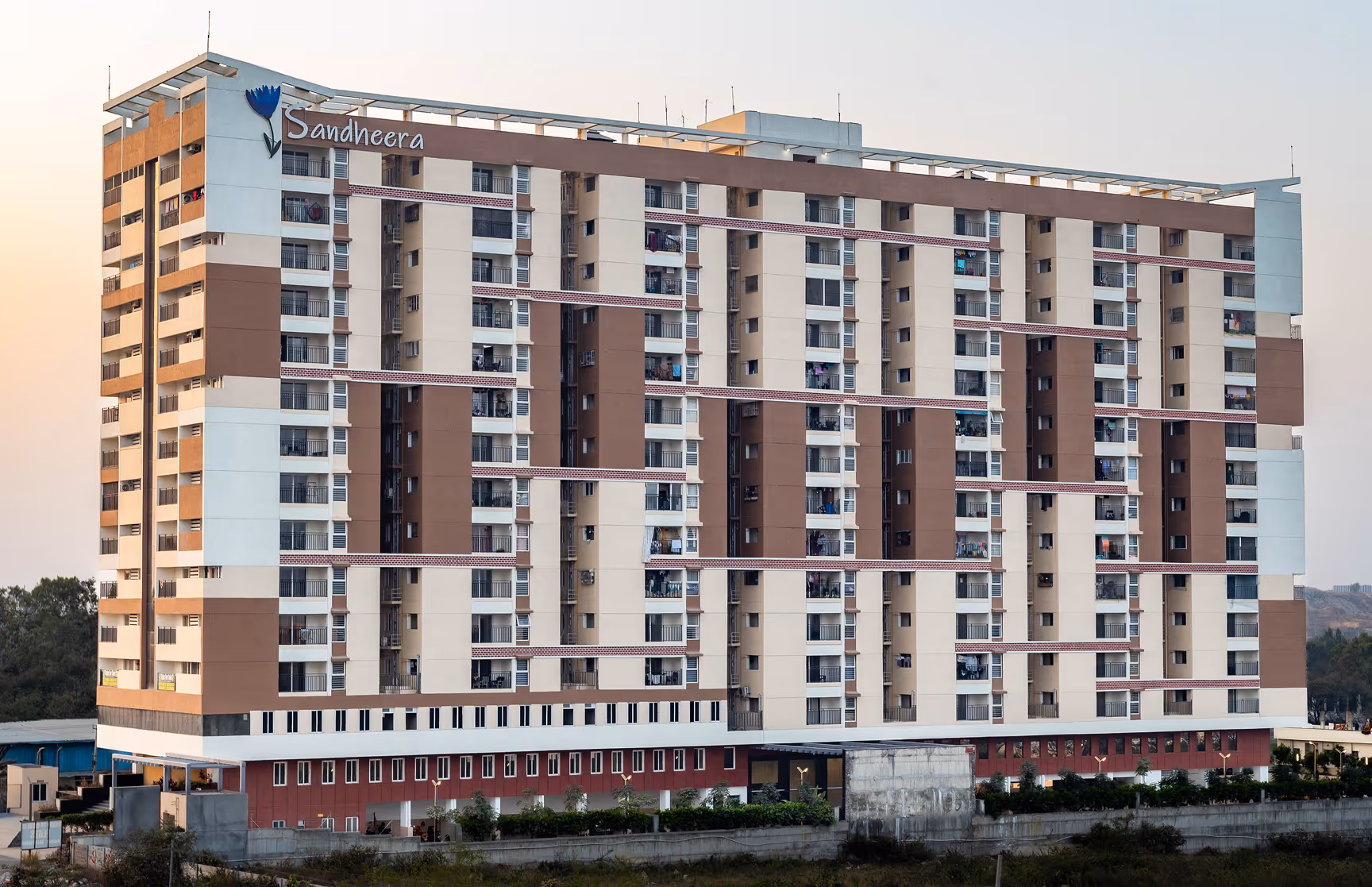 Multi-story residential building named Sandheera with beige and brown exterior during daytime.