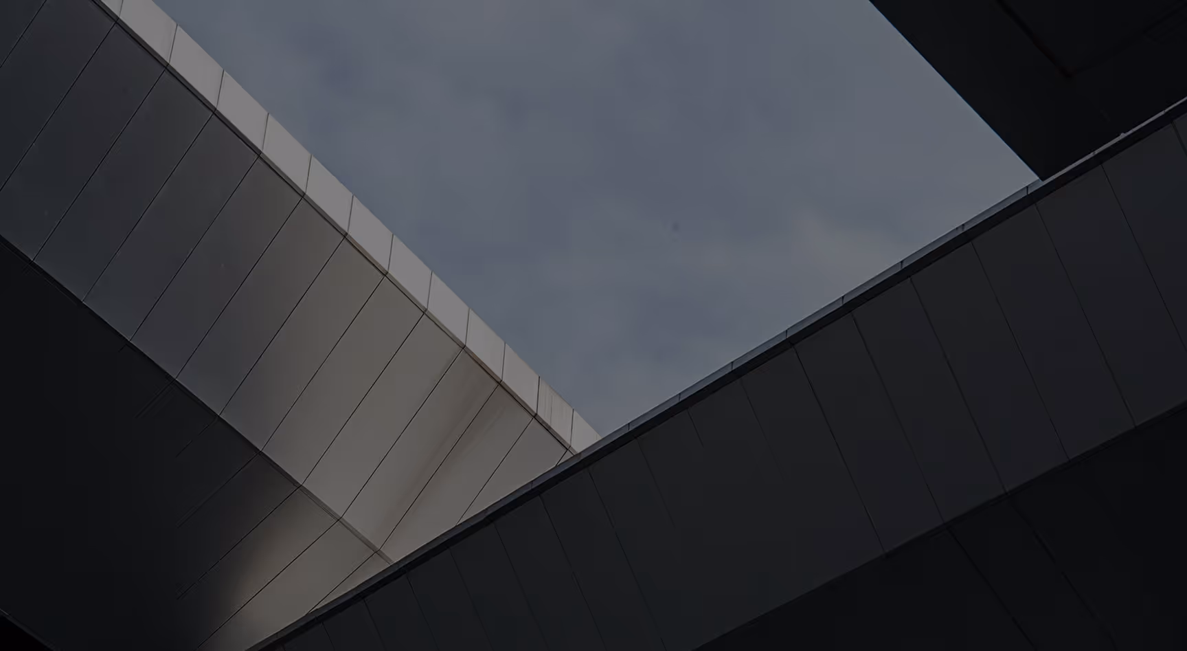 Gray and black modern building panels forming an abstract geometric frame against a cloudy sky.