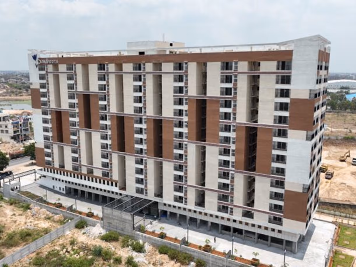 Large multi-story modern residential building with brown and white exterior panels under a cloudy sky.