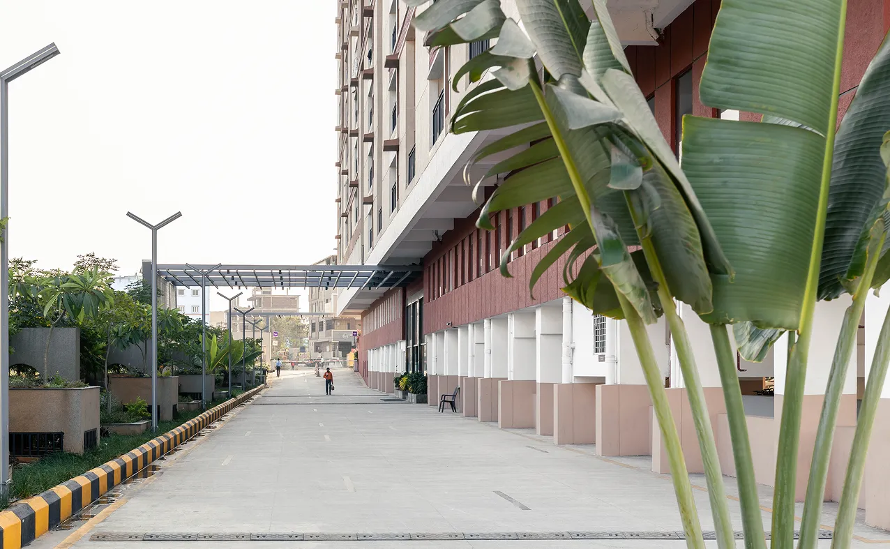 Modern building with pedestrian walkway, green plants, and a person walking in the distance.