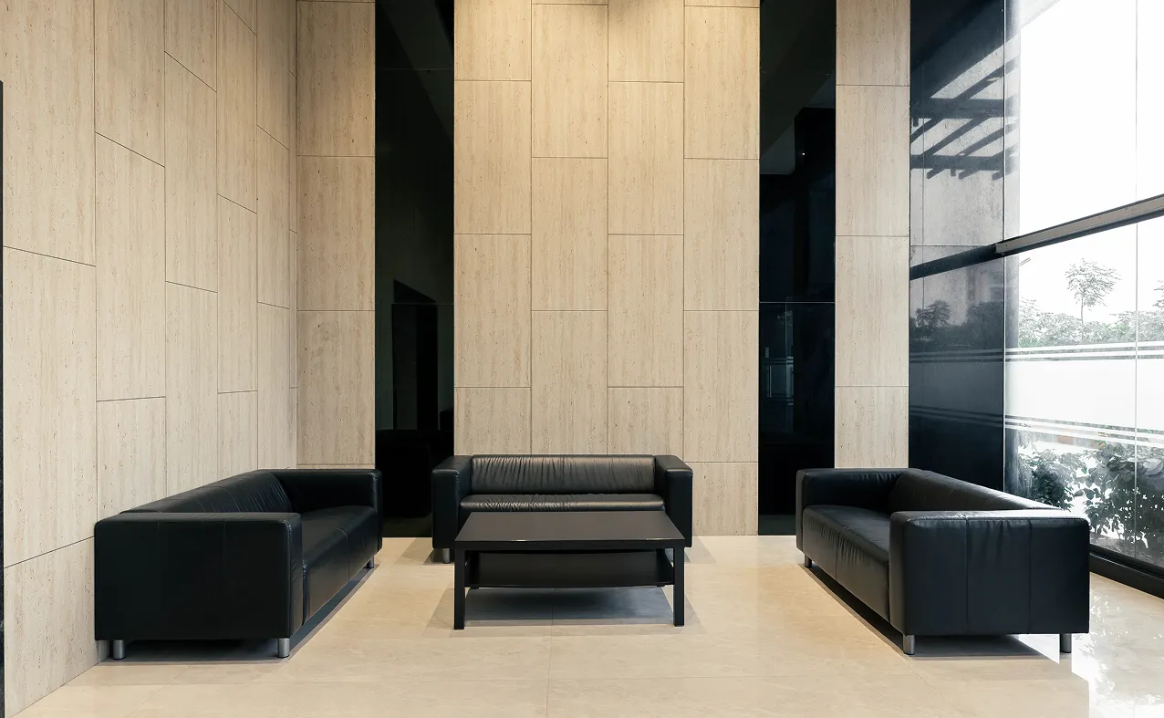Modern seating area with three black leather sofas and a black coffee table in a beige tiled room.