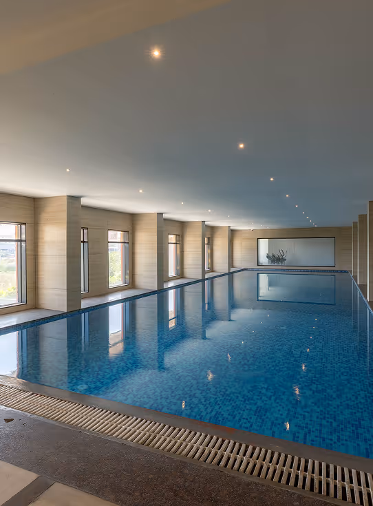 Indoor swimming pool with blue tiles, large windows, and recessed ceiling lights.