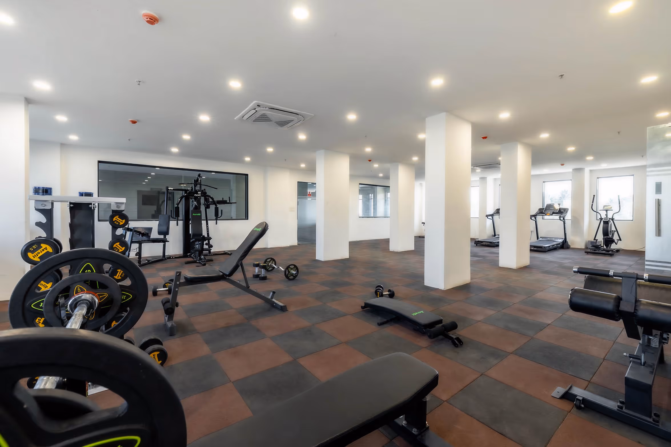 Spacious gym with weight benches, dumbbells, treadmills, elliptical, and multi-use workout machine.
