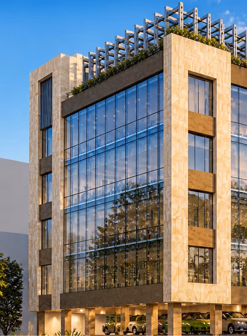 Modern multi-story building with large glass windows, beige frame, rooftop greenery, and parked cars below.