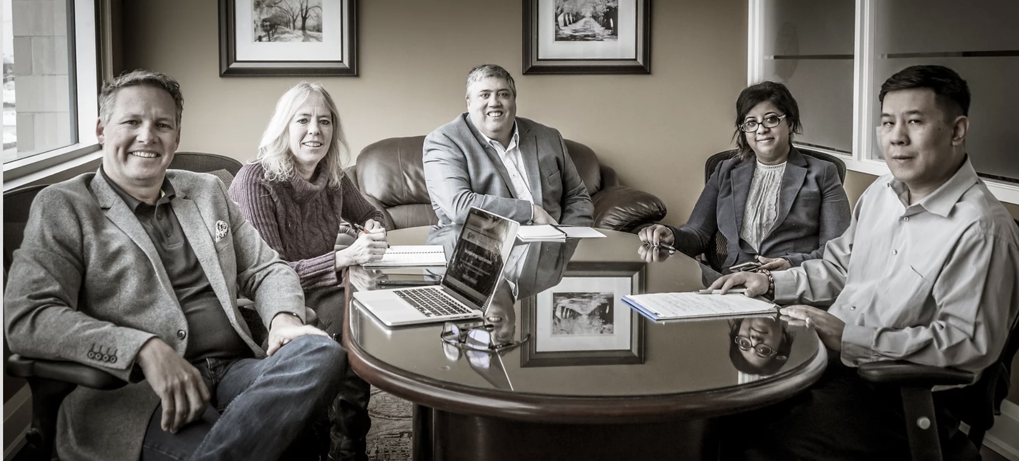 The team at Aria Benefits pose smiling around a big table in a meeting room. Robin Bailey is at the far left.