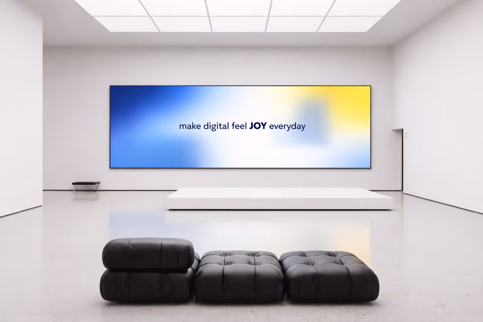 Minimalist room with black cushioned seats facing a large screen saying make digital feel JOY everyday.