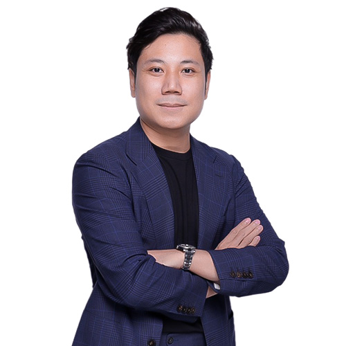 Confident man in a blue checkered blazer and black shirt with arms crossed against white background.