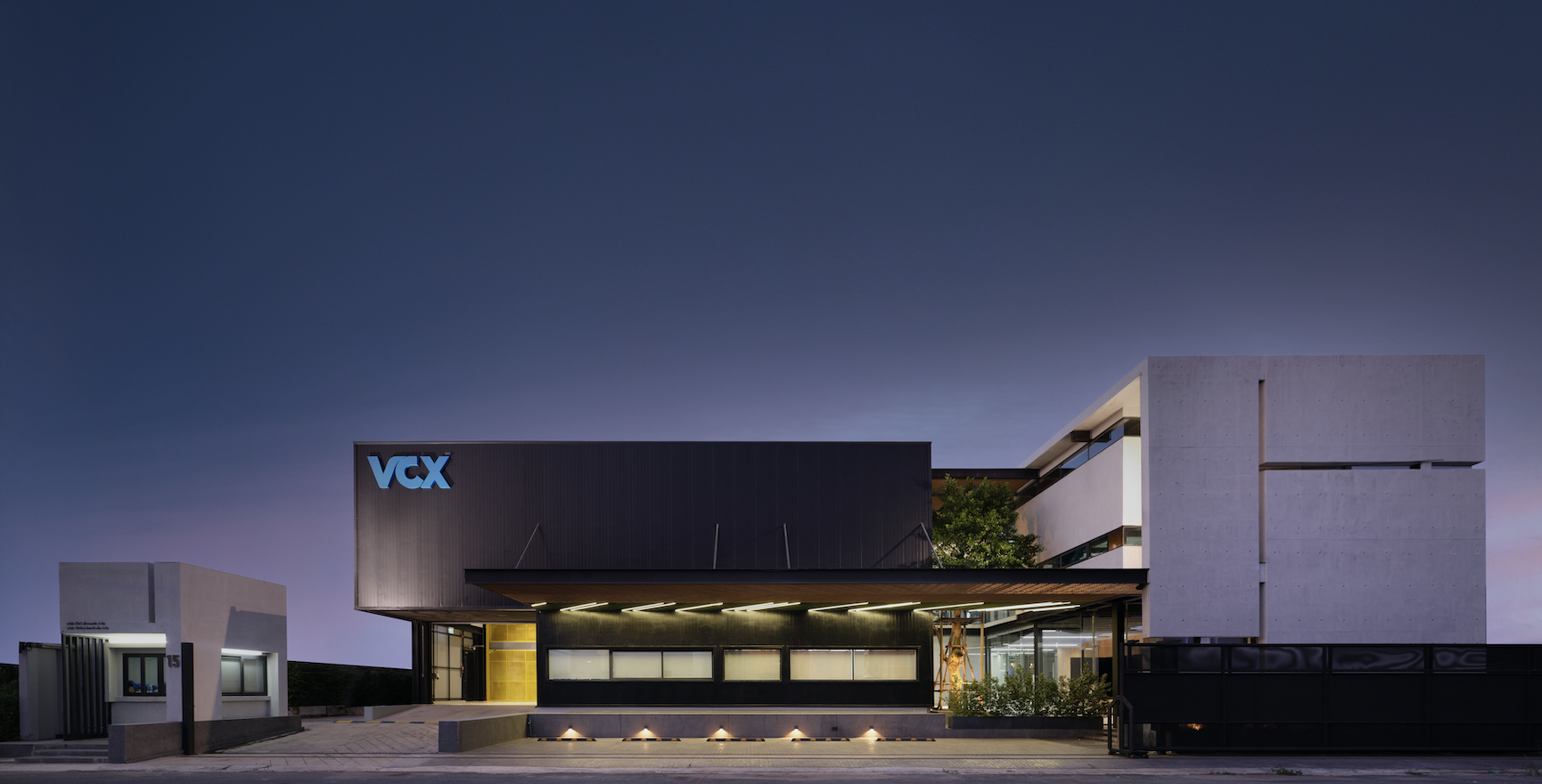 Modern building with VCX logo lit at dusk, showing clean lines, windows, and greenery.