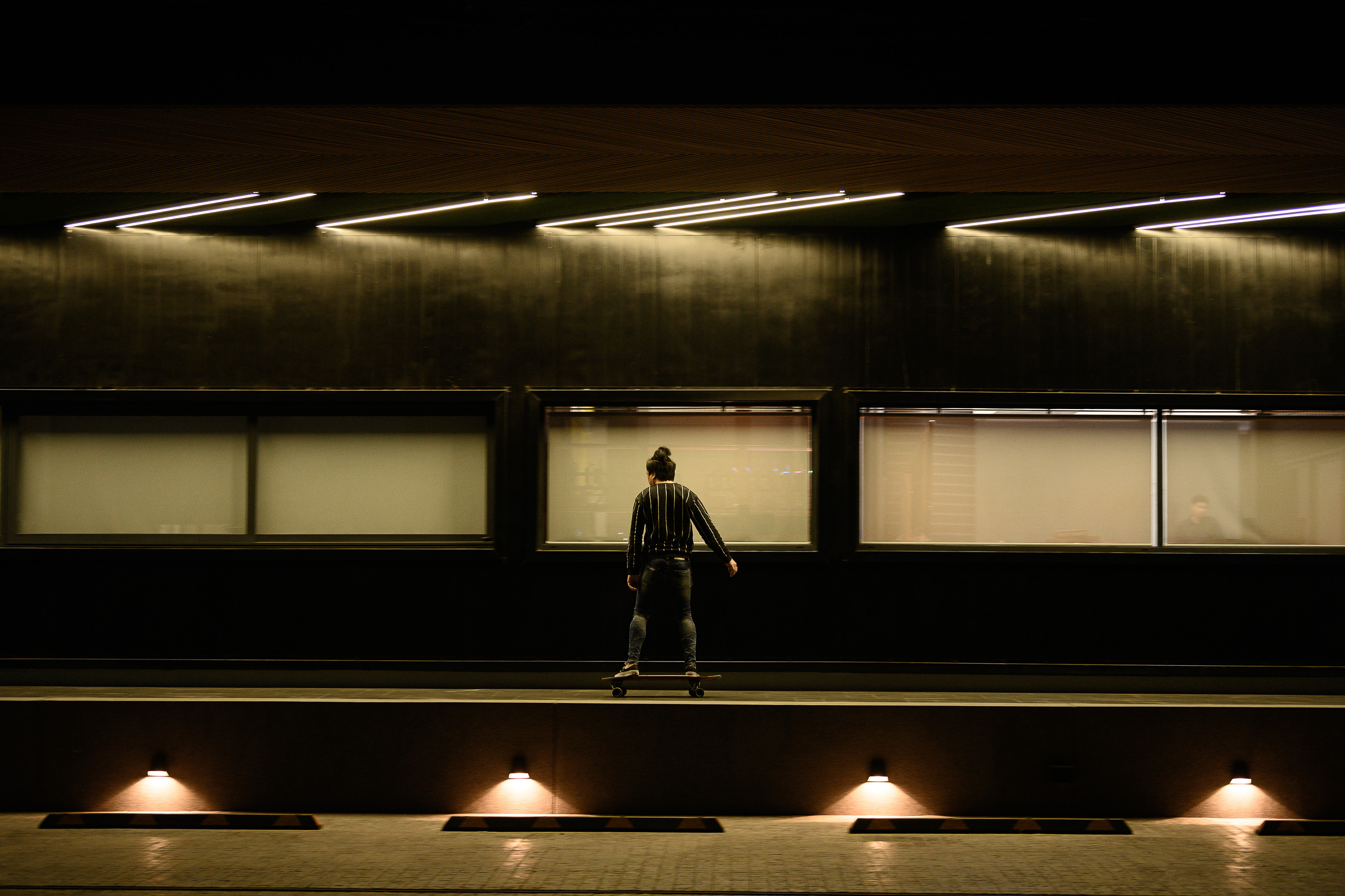 Person skateboarding on an elevated platform in dimly lit urban setting at night.
