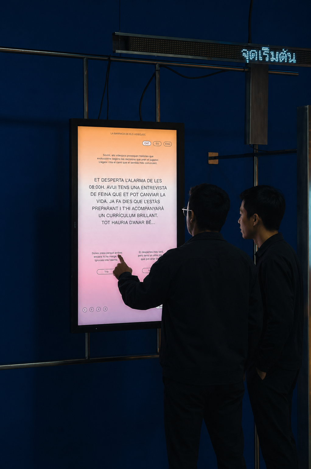 Two men interacting with an illuminated touchscreen display mounted on a dark blue wall.