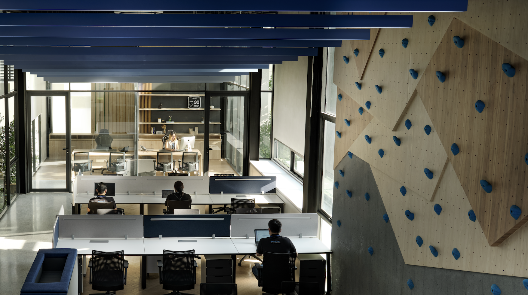 Modern office with employees at desks and a woman working in a glass-walled conference room.