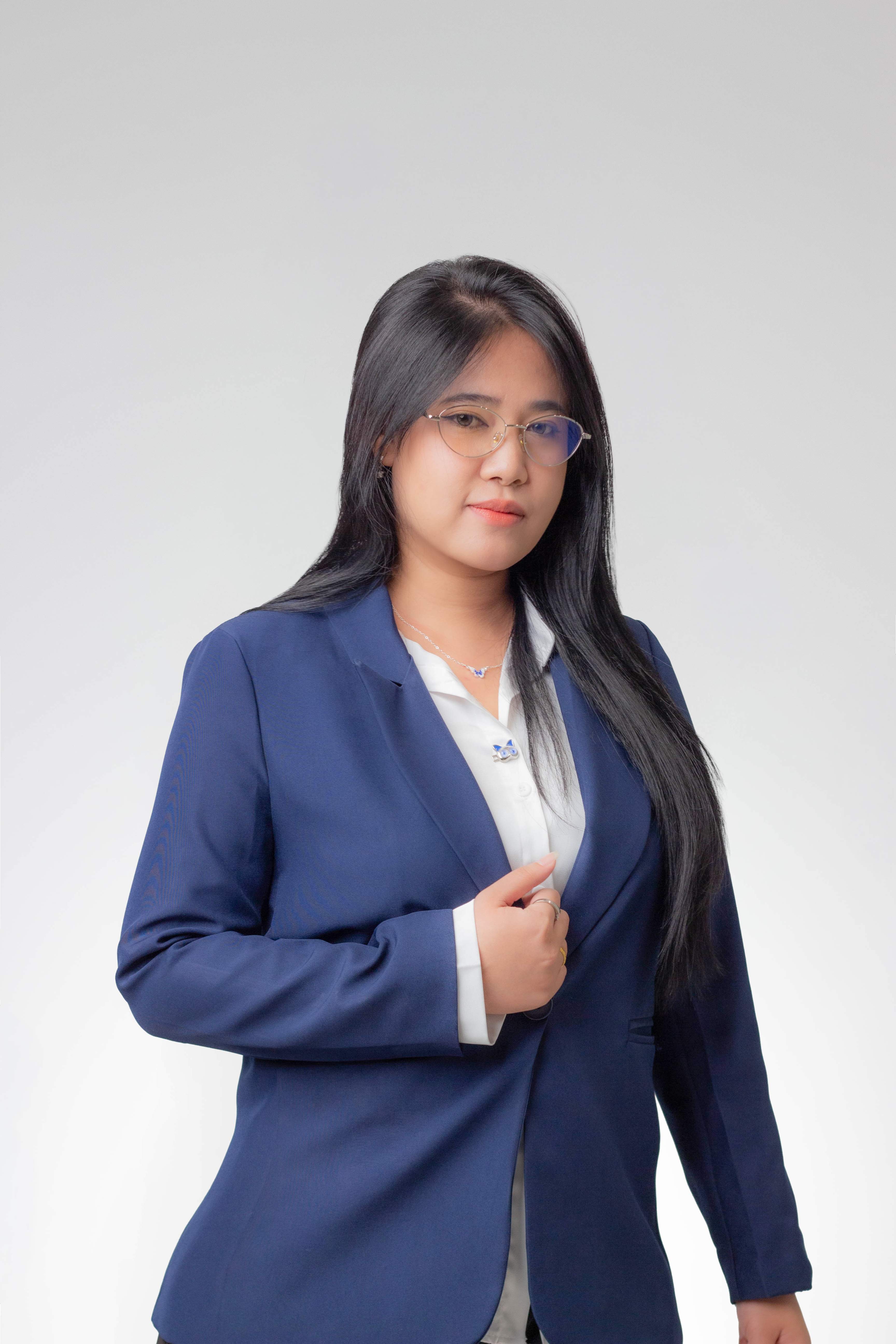 Woman with long black hair and glasses wearing a navy blazer over a white blouse.