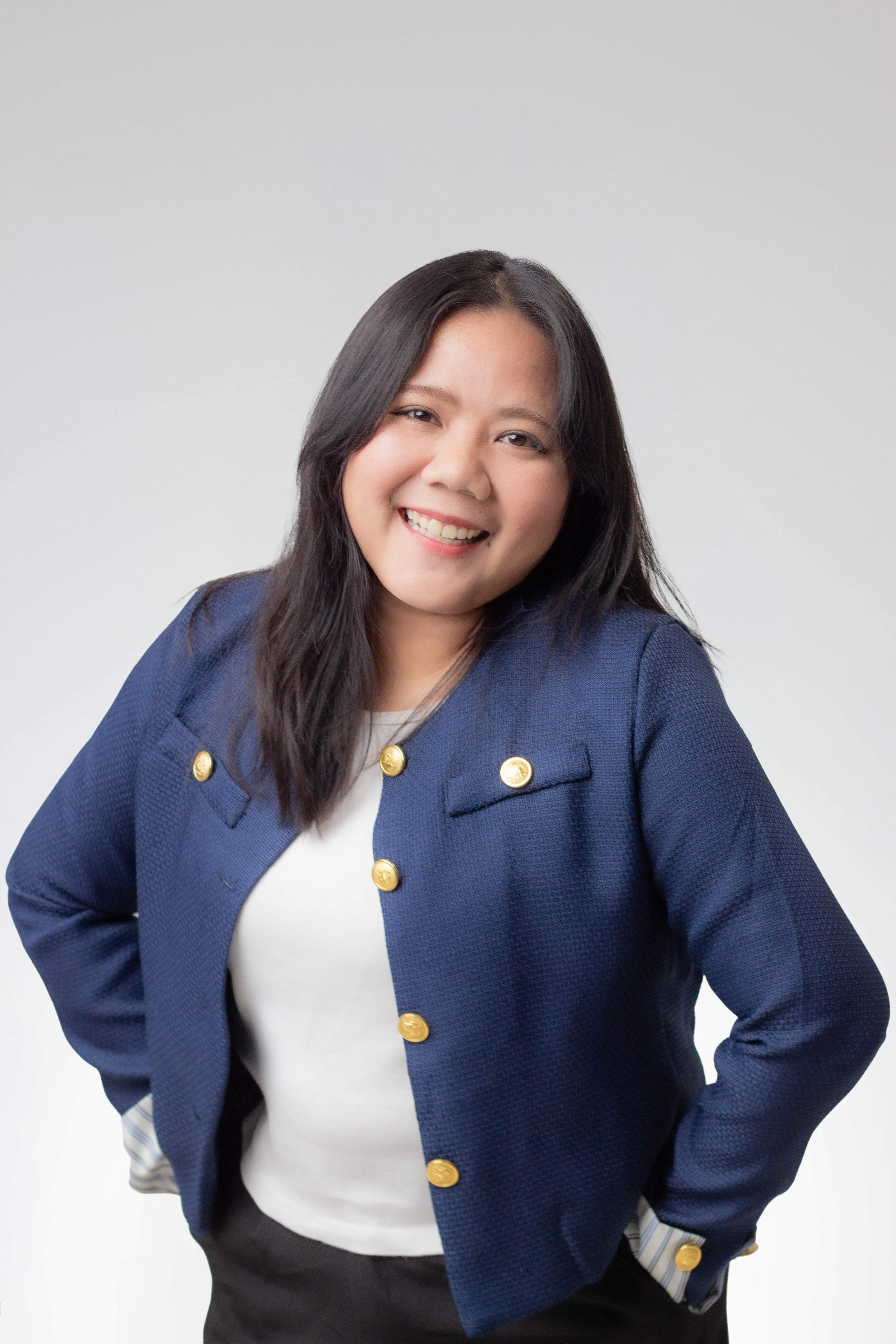 Smiling woman with long dark hair wearing a blue jacket with gold buttons and white shirt.