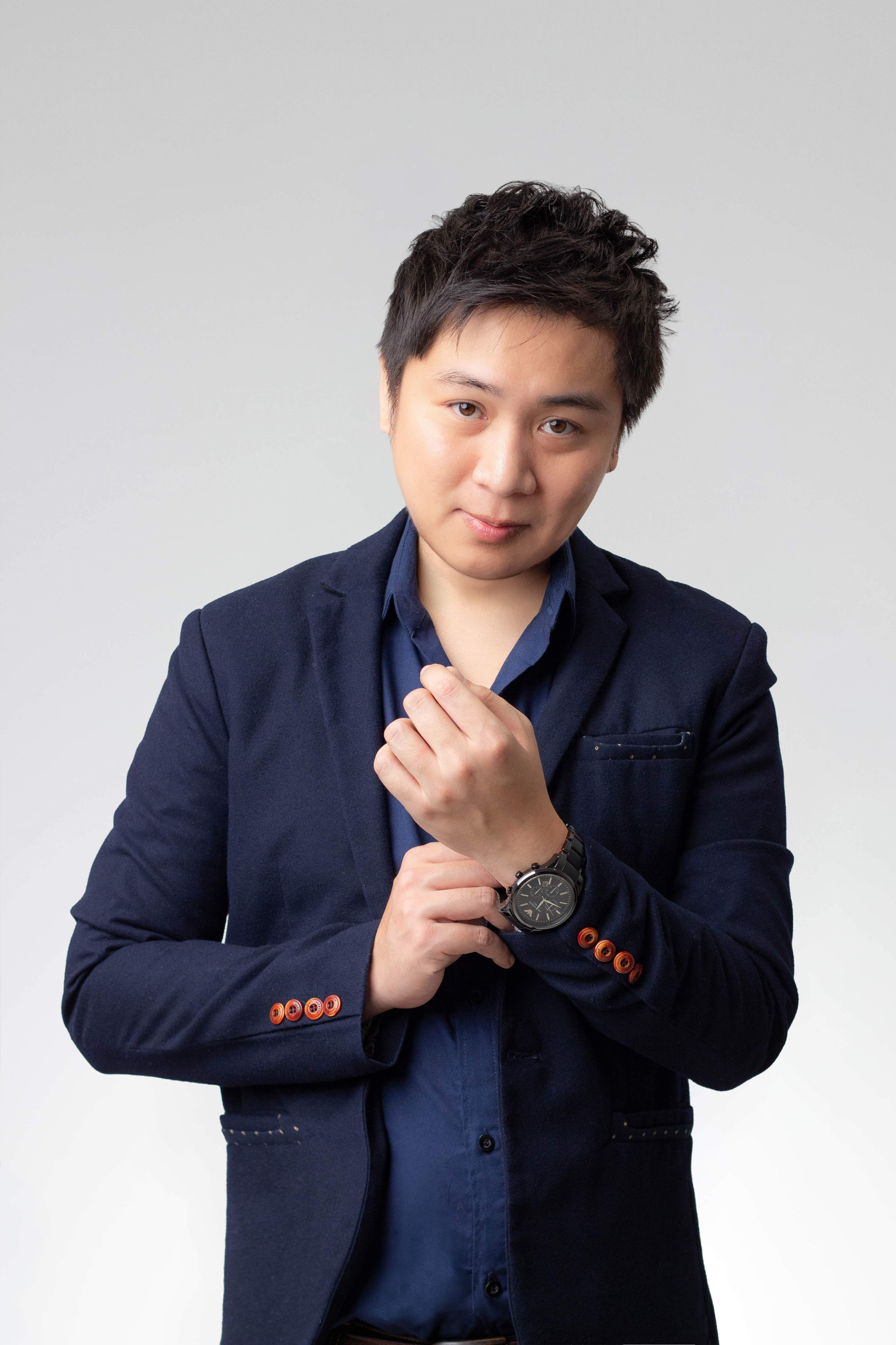 Man in navy blazer adjusting his wristwatch, looking at the camera with a neutral expression.