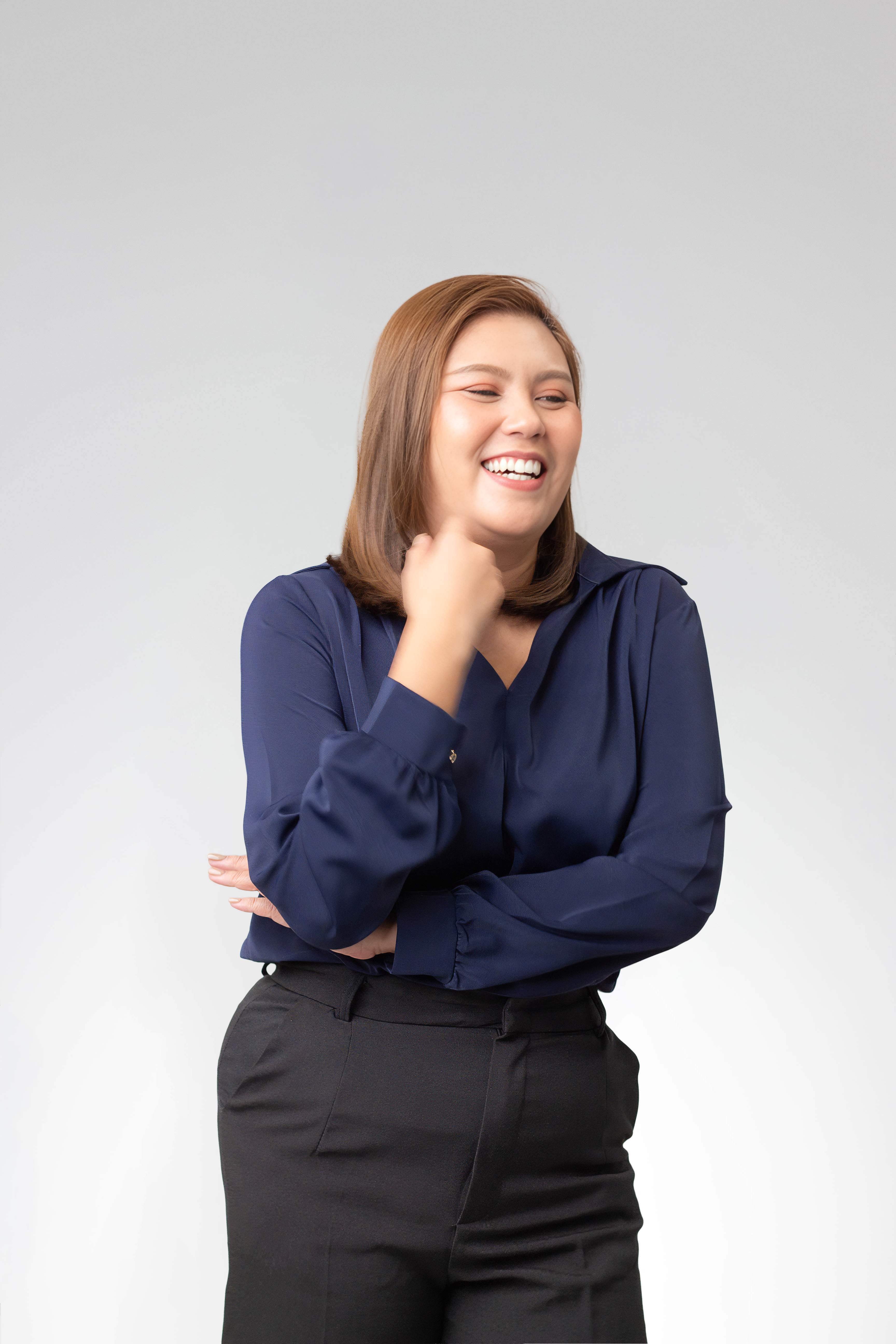 Smiling woman in navy blouse and black pants with arms crossed and hand near her face.
