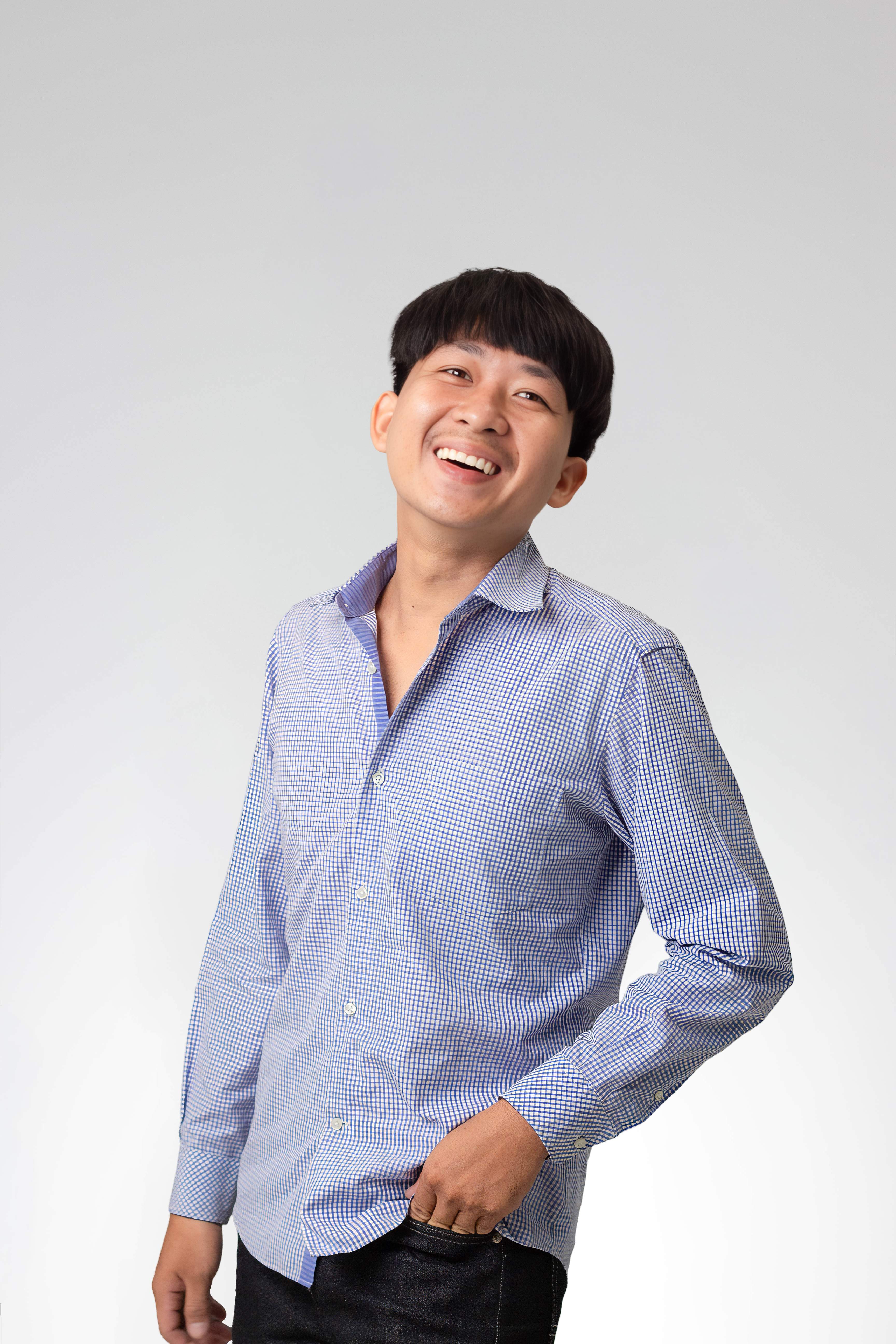 Smiling young man in a blue checkered shirt with hand in pocket on white background.