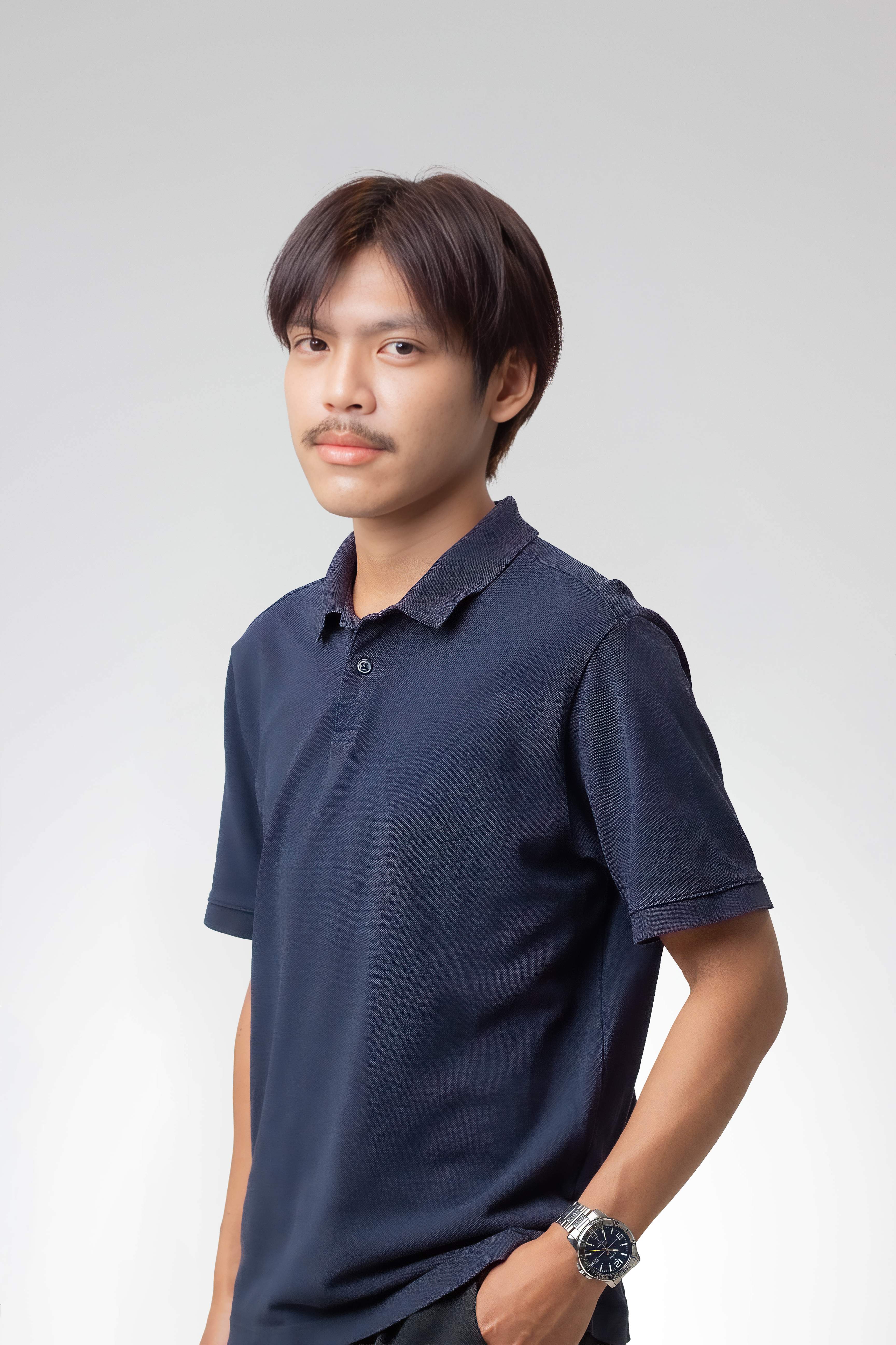 Young man with mustache wearing a navy polo shirt and a wristwatch with hand in pocket.