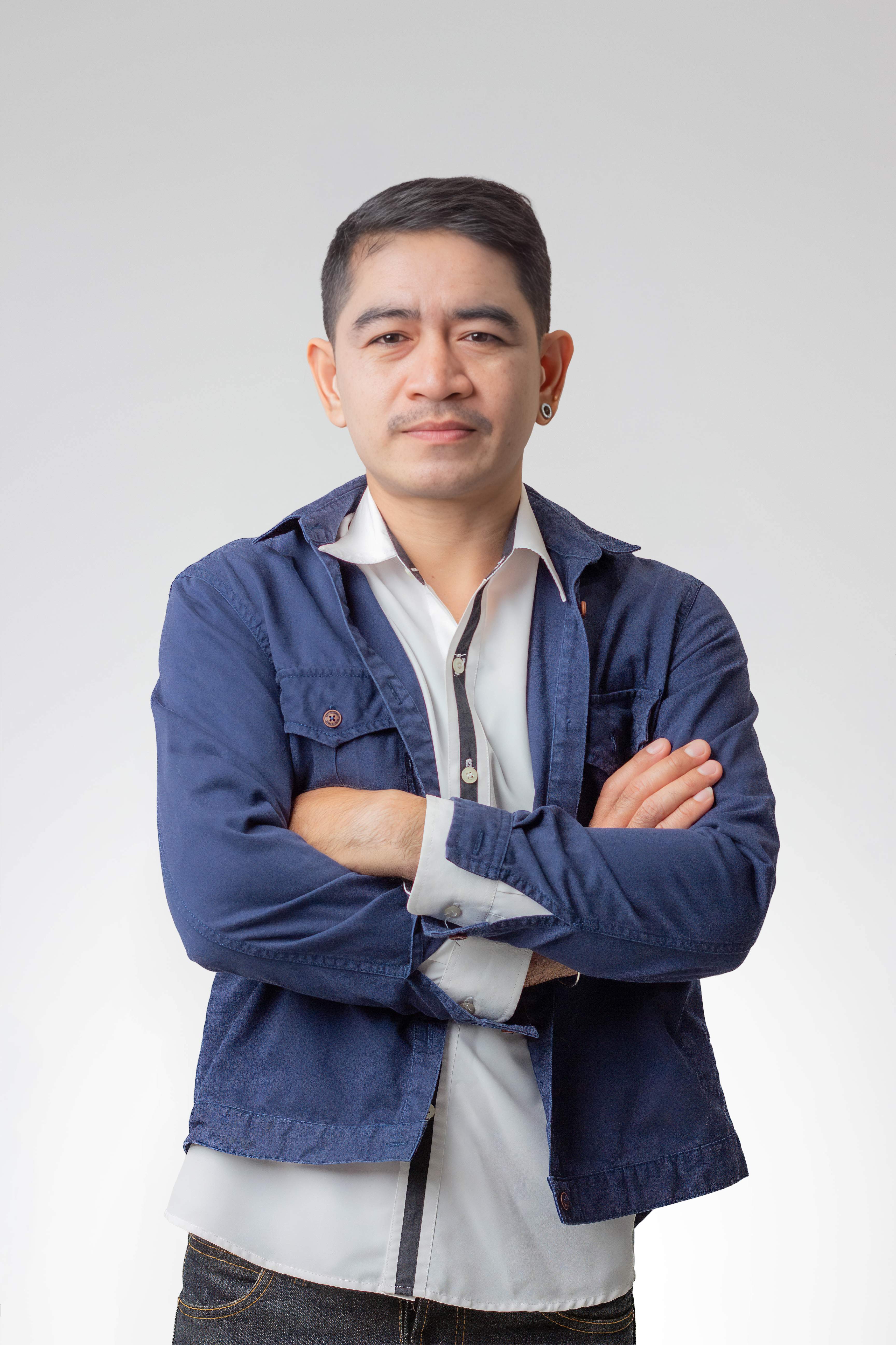 Man wearing a white shirt and blue jacket standing with arms crossed against a plain background.