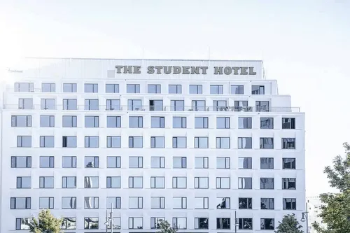 Helles modernes Gebäude mit vielen Fenstern und dem Schriftzug "THE STUDENT HOTEL" auf dem Dach.