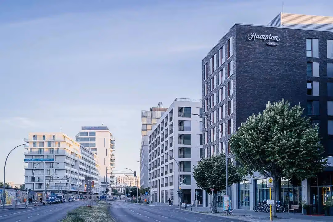 Straße mit modernen Wohn- und Geschäftsgebäuden, darunter ein Hampton by Hilton Hotel am Mercedesplatz Berlin.