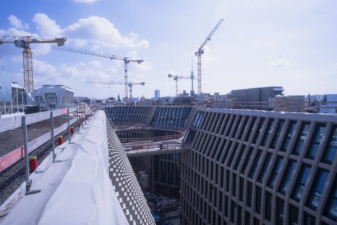 Blick auf Baustelle am Tacheles Berlin mit mehreren Kränen und einem großen, runden Gebäudekomplex bei klarem Himmel.