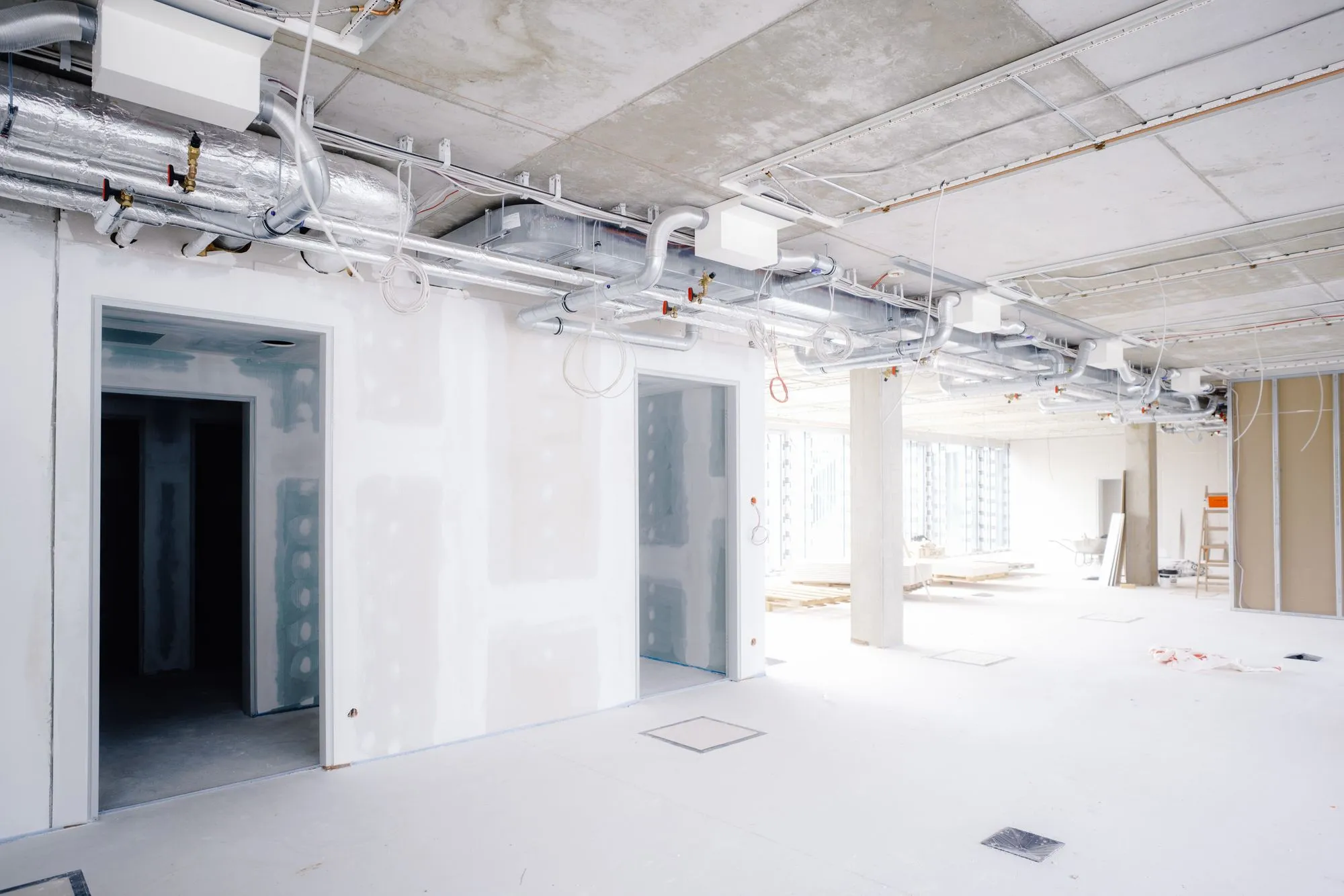 Baustelle im Rohbau mit sichtbaren Lüftungsrohren und unvollständigen Wänden.