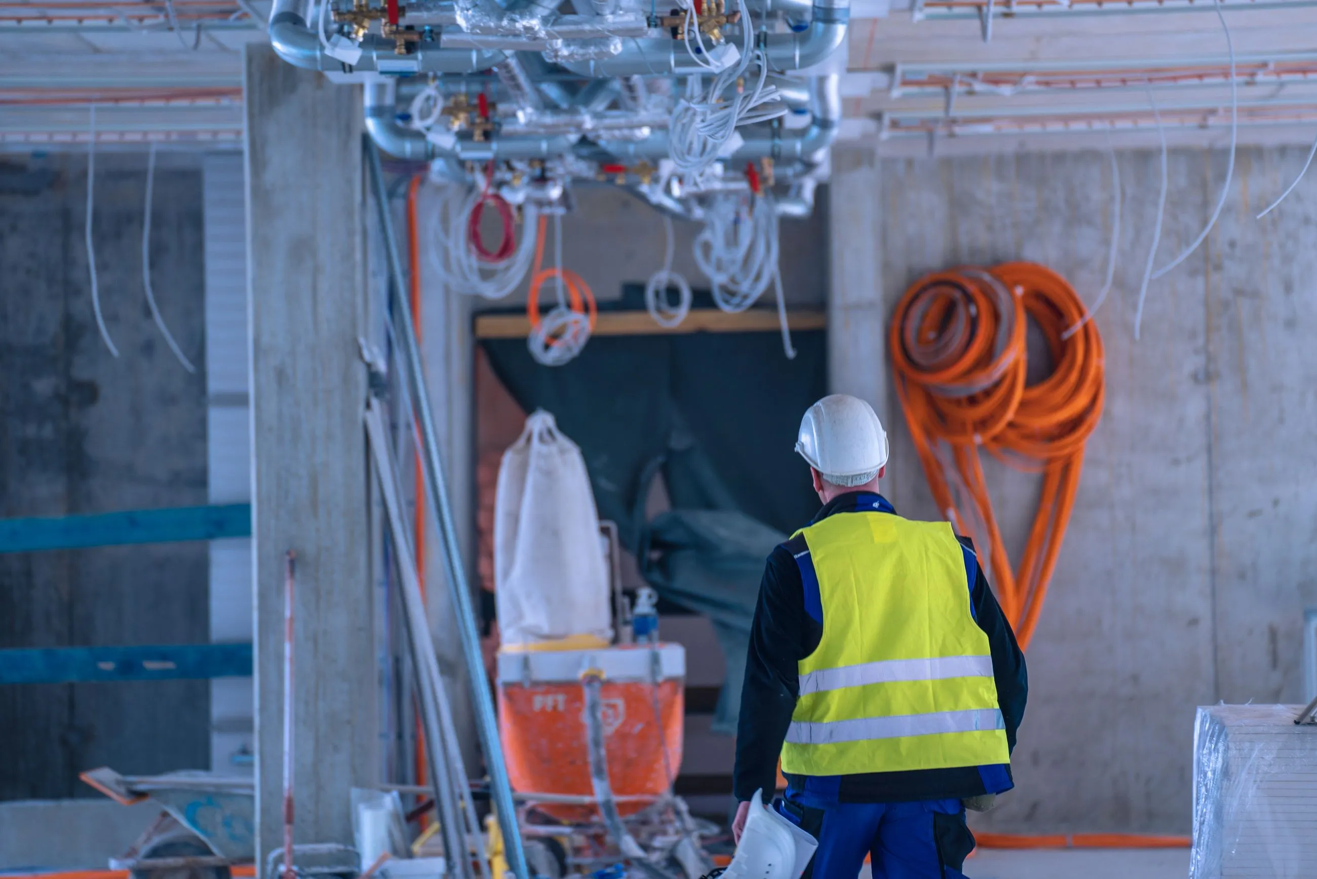 Projektleiter von IB Walther Berlin mit weißem Helm und gelber Warnweste in einer Baustelle mit Rohren und Baumaterialien.