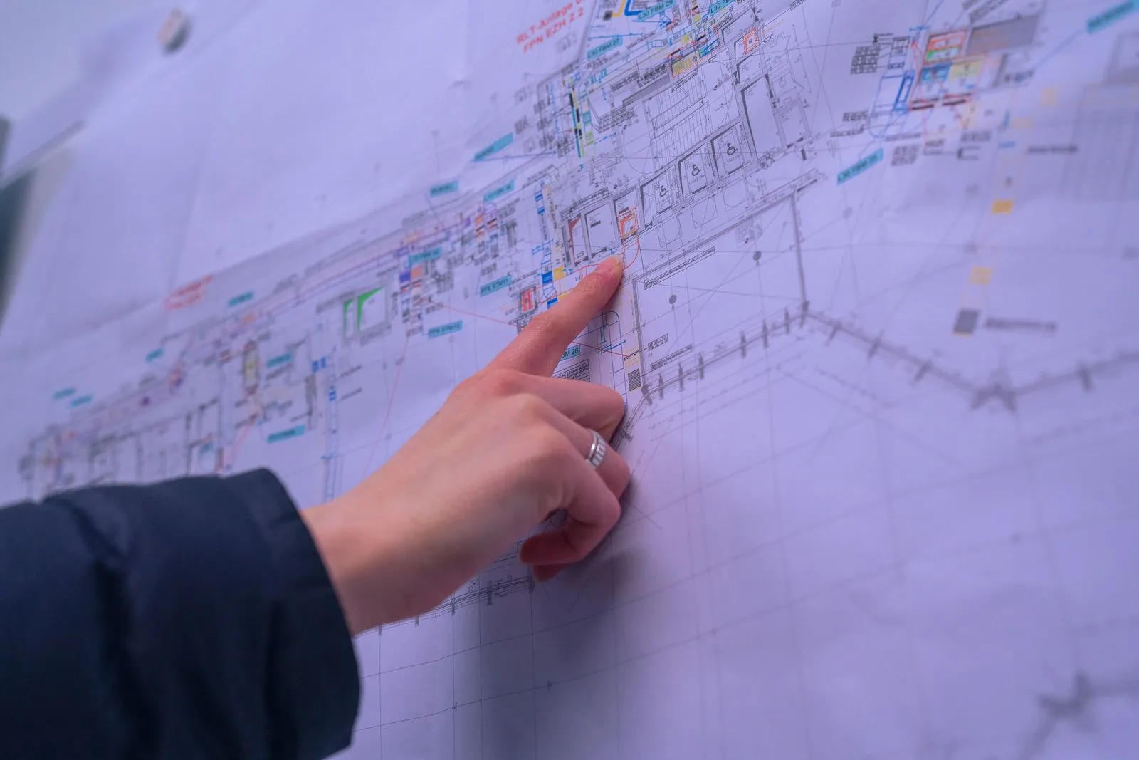 Eine Hand zeigt auf einen Bereich eines detaillierten architektonischen Bauplans an der Wand.