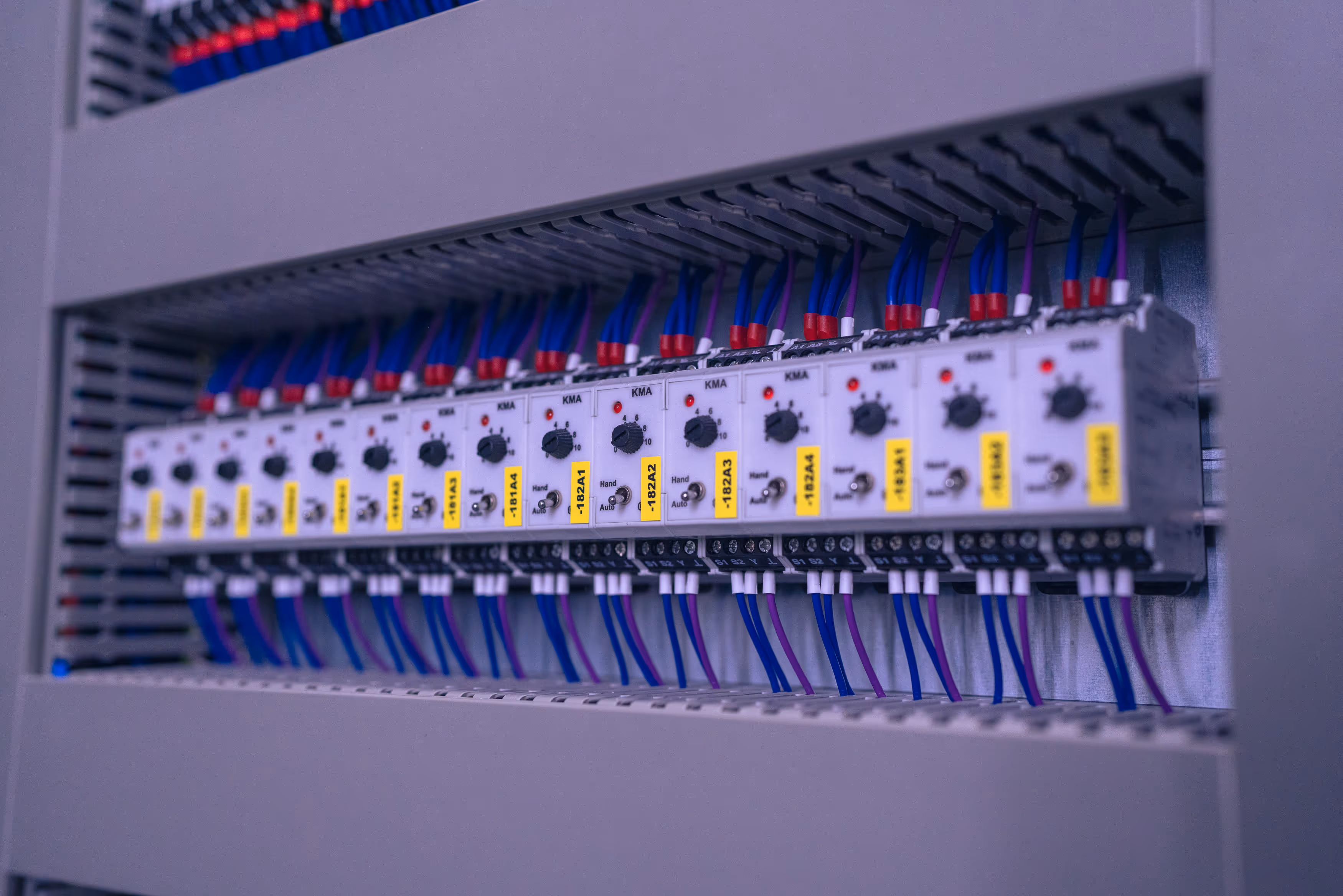 Reihe von elektronischen Steuerungsmodulen mit blauen und violetten Kabeln in einem Schaltschrank.