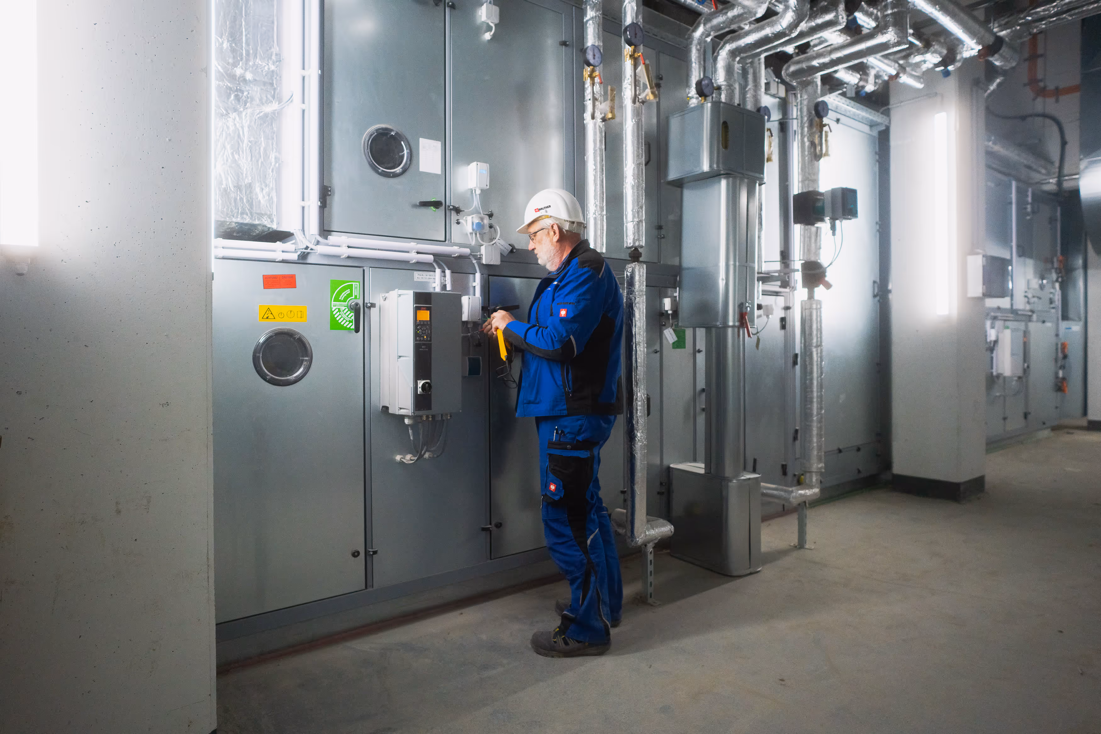 IB Walther Techniker in blauer Arbeitskleidung und Schutzhelm überprüft Steuerung in einer technischen Anlage.