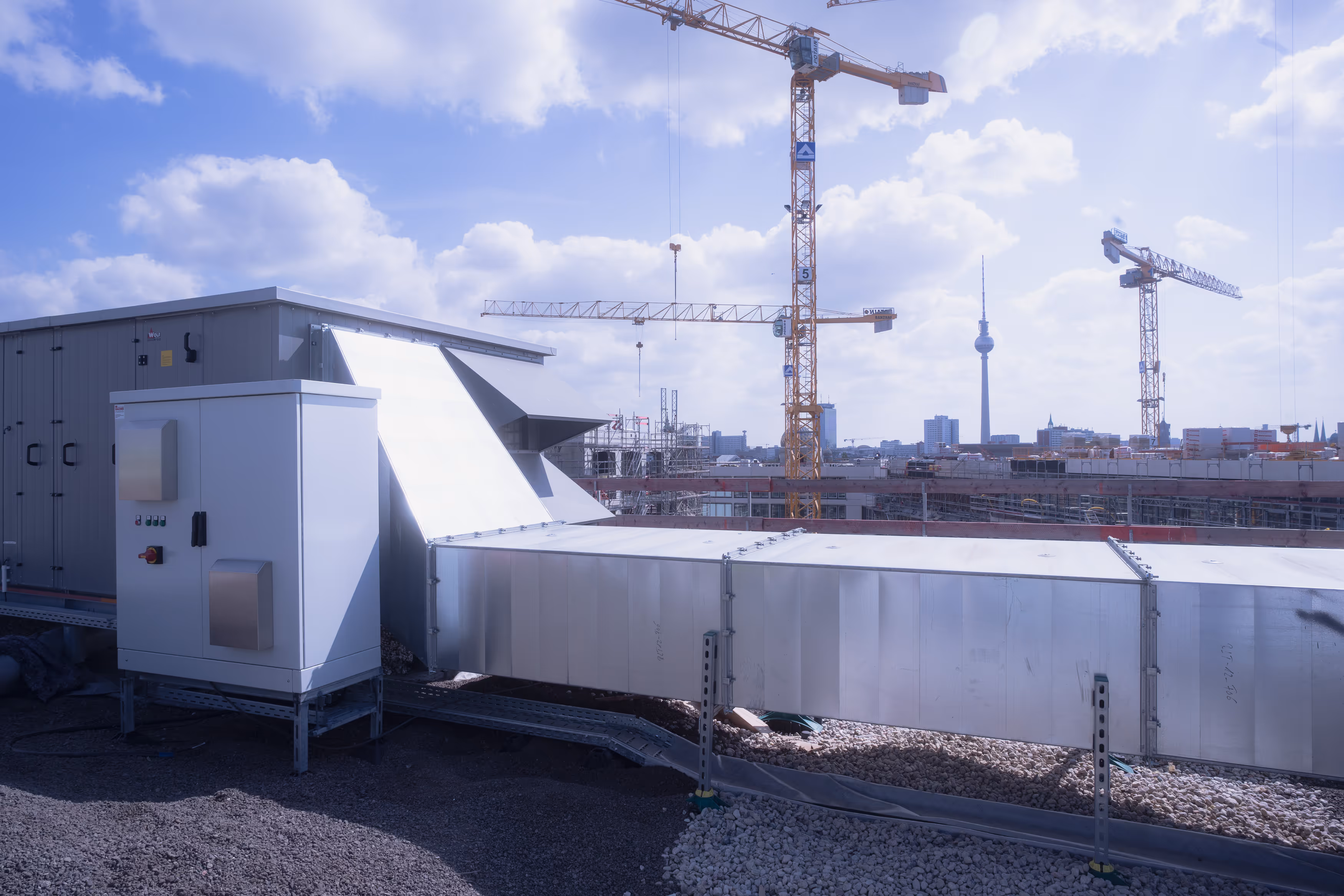 Industrieanlage auf einem Flachdach mit Baukranen und dem Berliner Fernsehturm im Hintergrund.