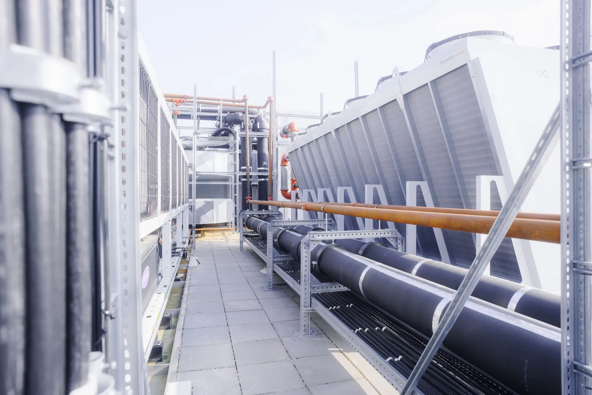 Industrielle Lüftungs- und Kühlausrüstung mit großen Rohren und Metallstrukturen auf einer Terrasse.