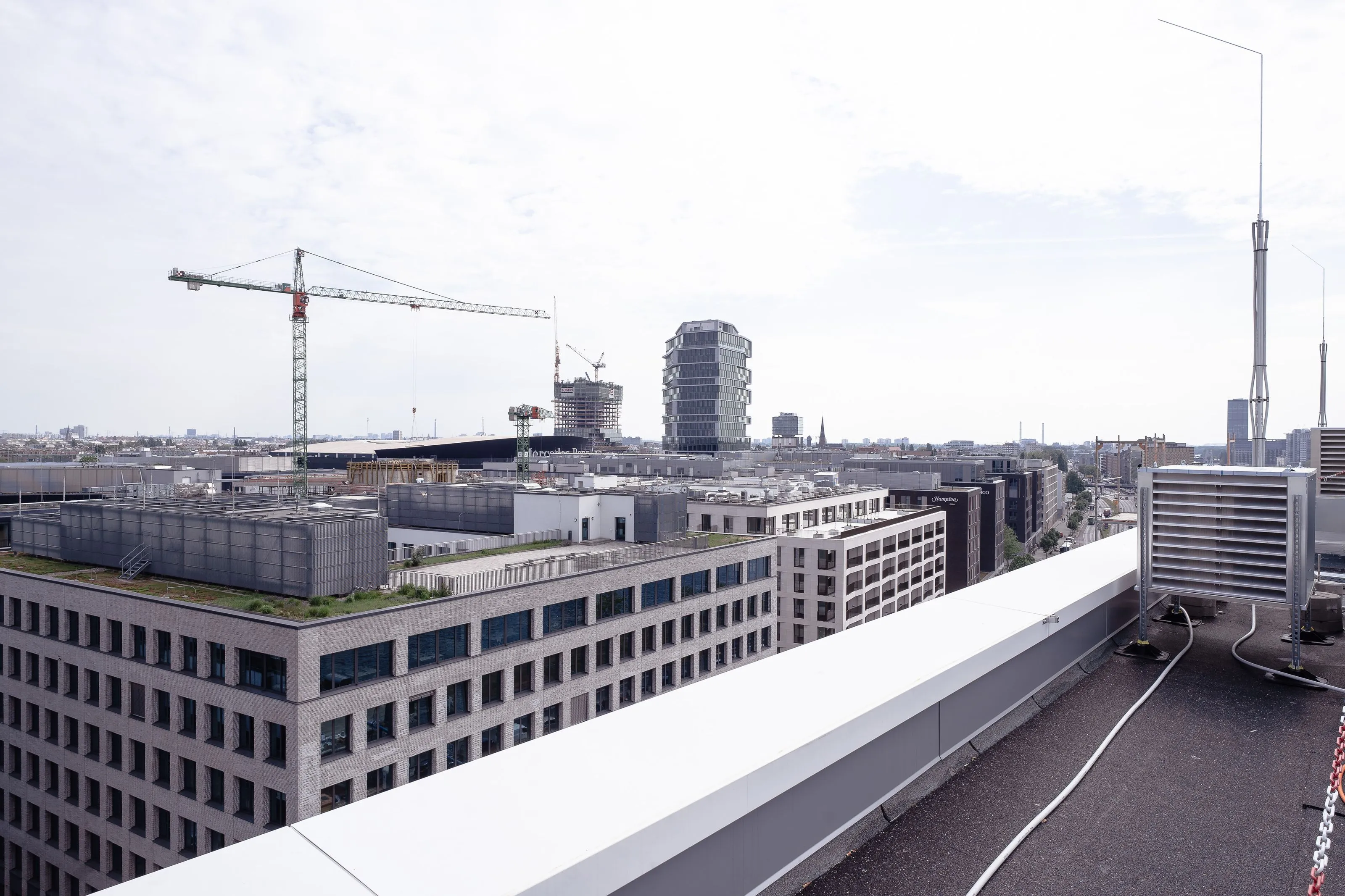 Städtische Skyline mit modernen Bürogebäuden, einem Kran und Luftanlagen auf einem Dach unter leicht bewölktem Himmel.