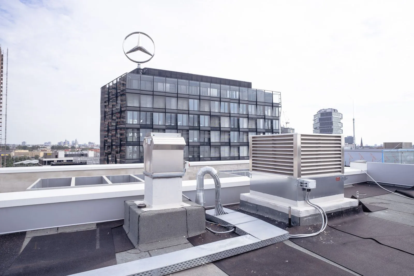 Dach mit Lüftungsanlagen und im Hintergrund ein modernes Gebäude mit großem Mercedes-Stern auf dem Dach.
