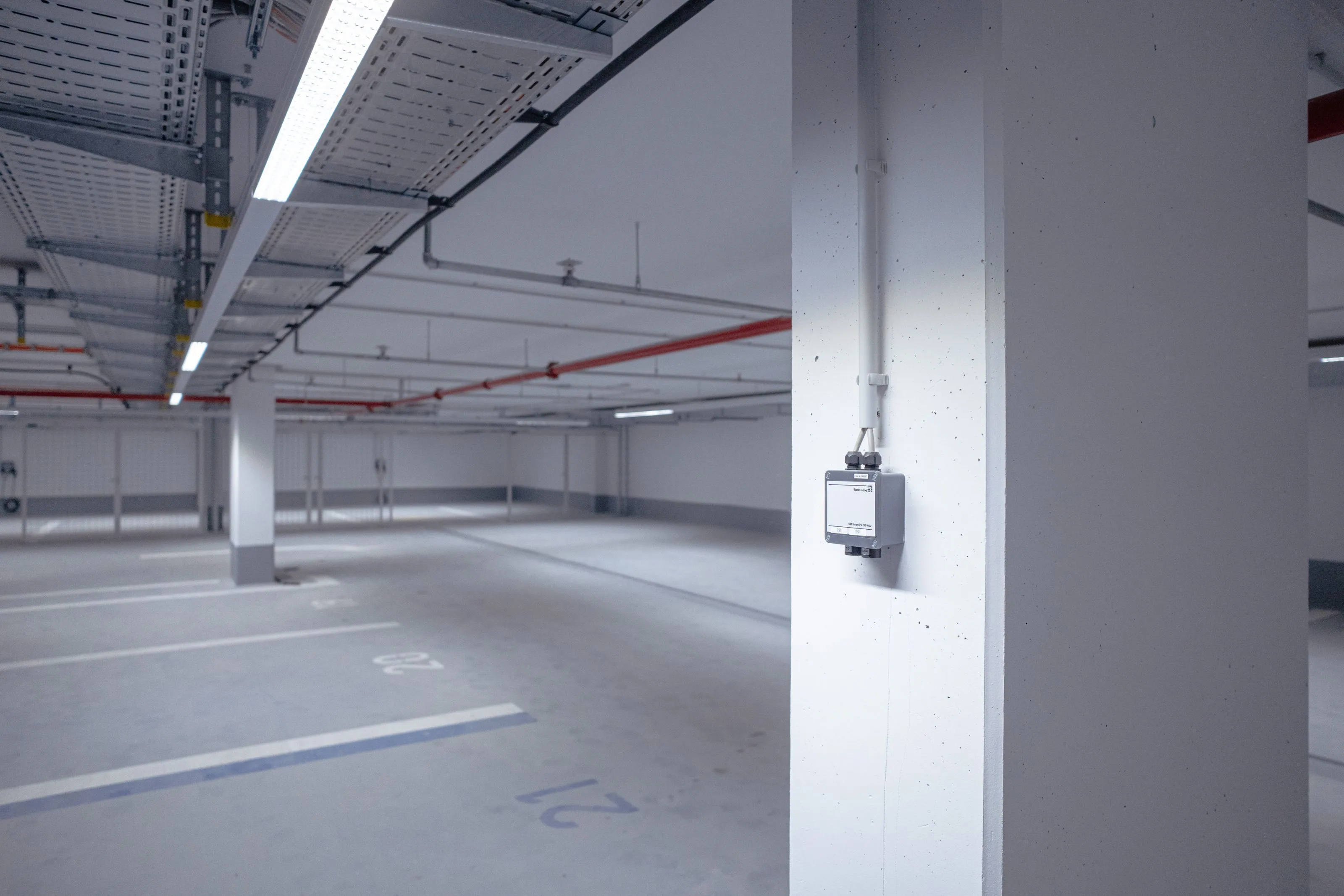 Leere Tiefgarage mit nummerierten Parkplätzen und weißem Pfeiler mit montiertem elektrischen Gerät.
