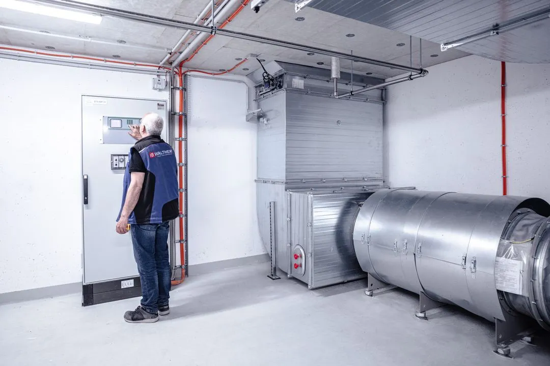 Techniker bedient ein Steuergerät in einem hellen, industriellen Raum mit großen Lüftungsrohren.