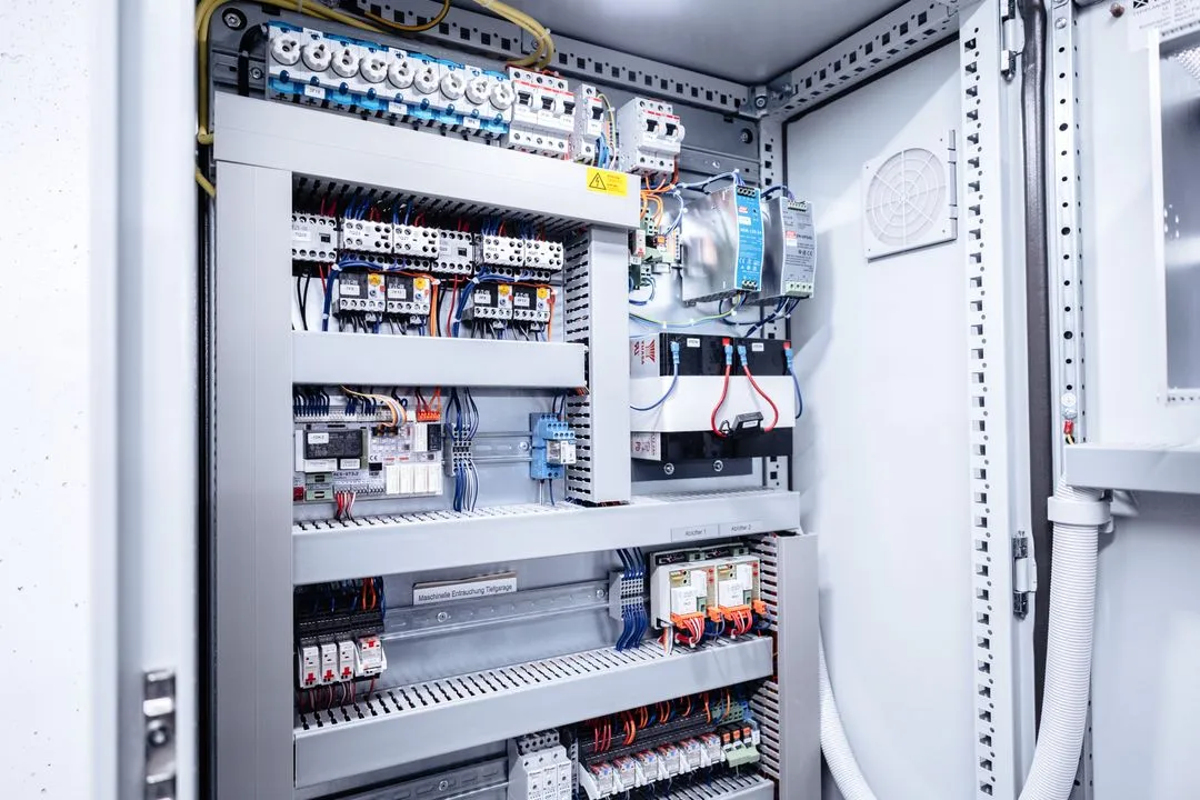 Geöffneter Schaltschrank mit verschiedenen elektrischen Steuerungs- und Sicherungskomponenten.