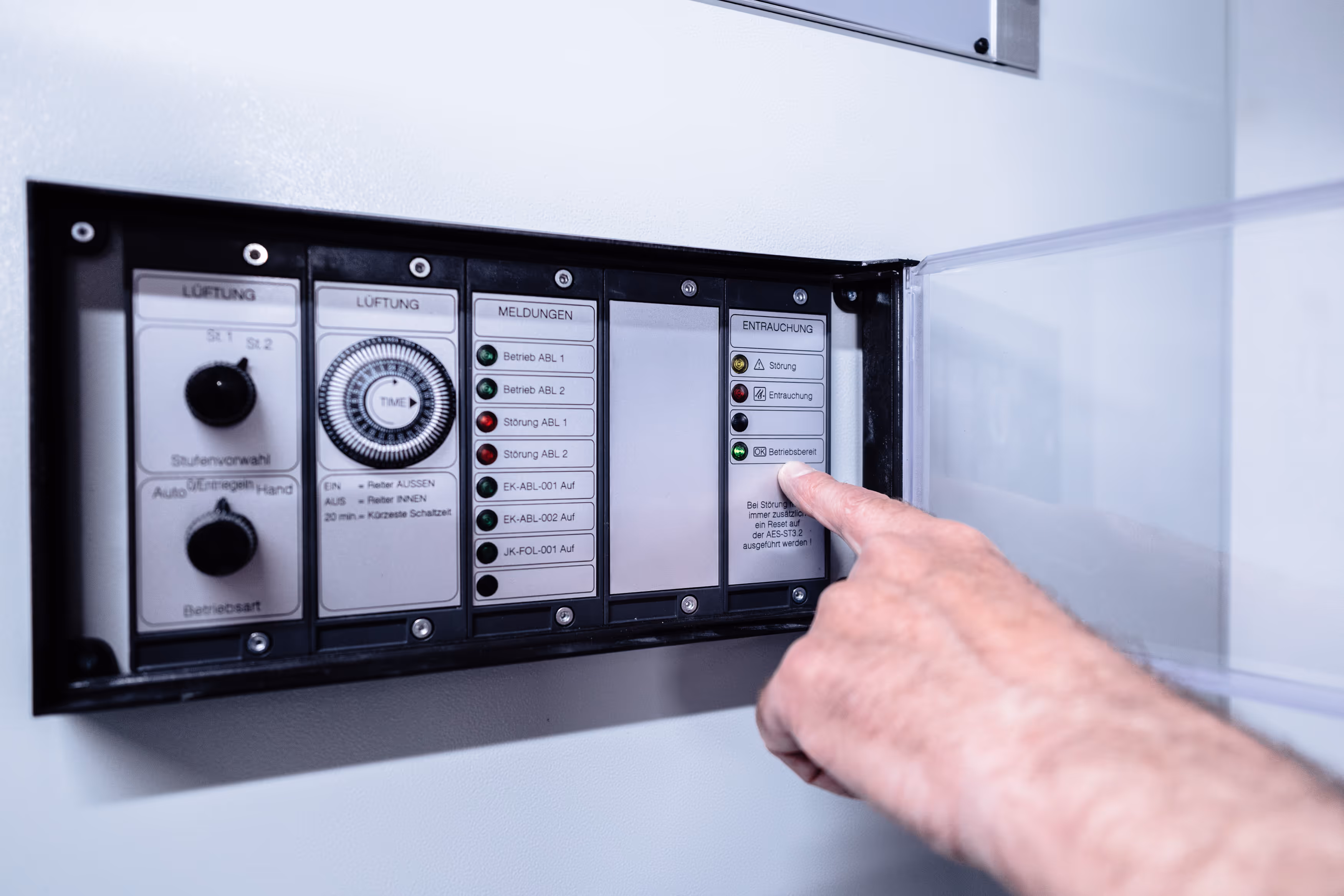 Hand tippt auf grünes Kontrolllämpchen für Betriebsbereit an einem Lüftungs- und Entrauchungssystem-Schaltkasten.