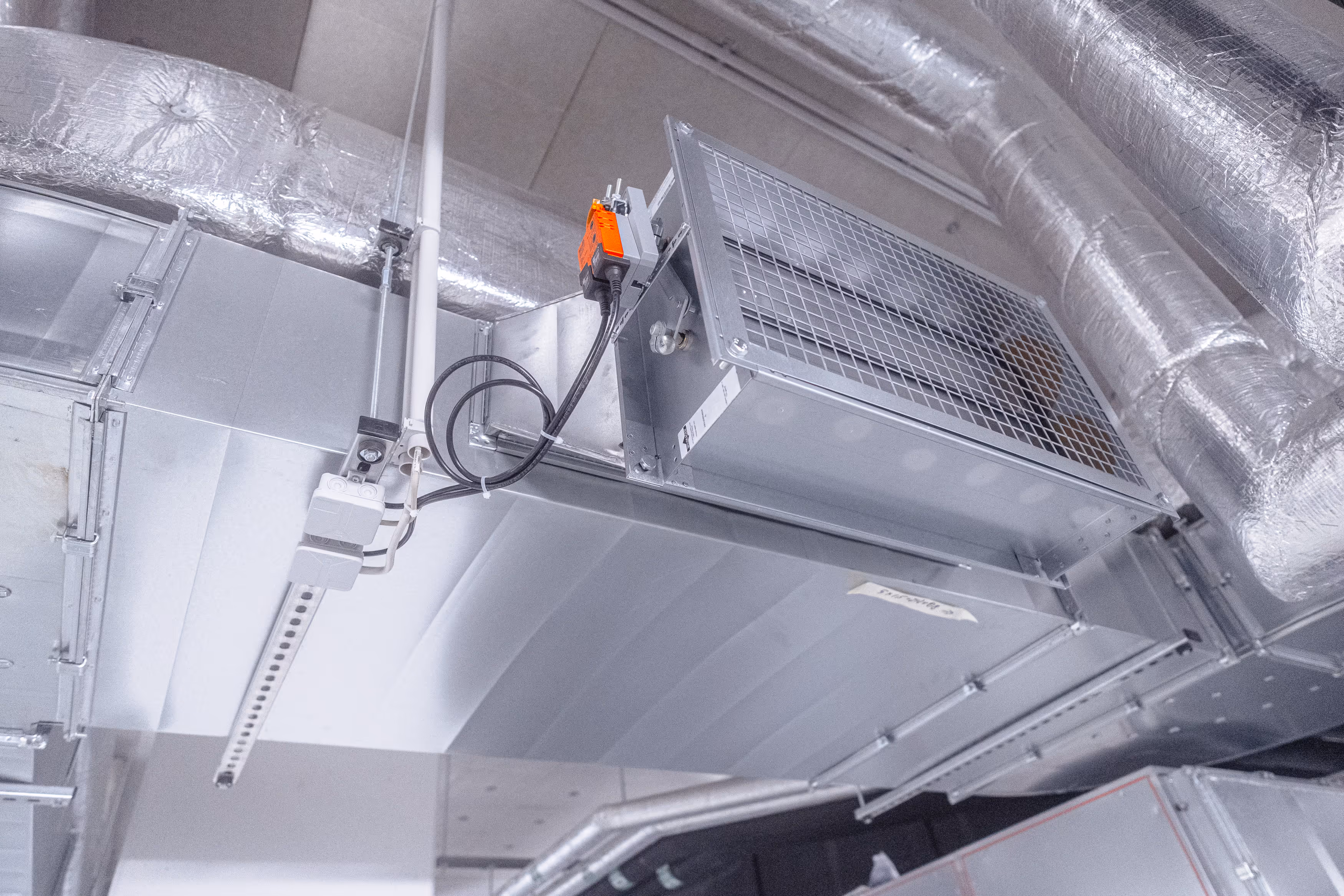 Decke mit metallischen Lüftungskanälen und isolierten Rohren in einem technischen Raum.