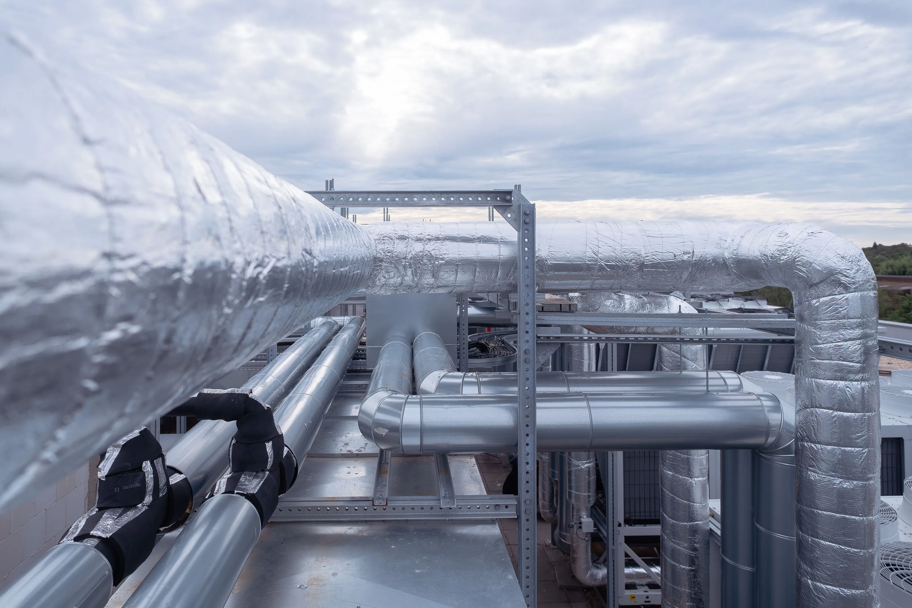 Isolierte silberne Rohrleitungen auf einem Industriegebäude unter bewölktem Himmel.