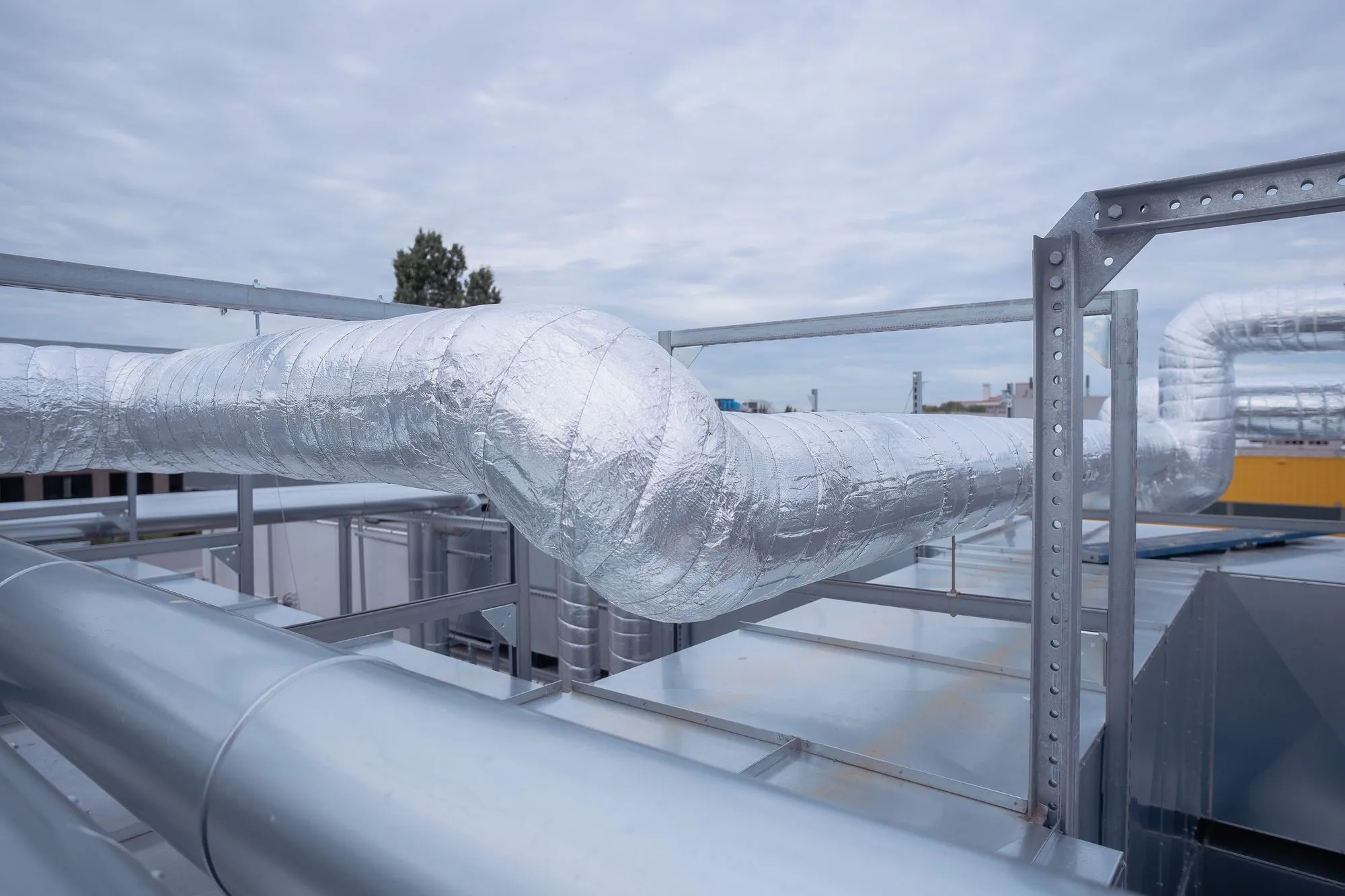 Isolierte und unisolierte Lüftungsrohre auf einem Gebäudedach unter bewölktem Himmel.