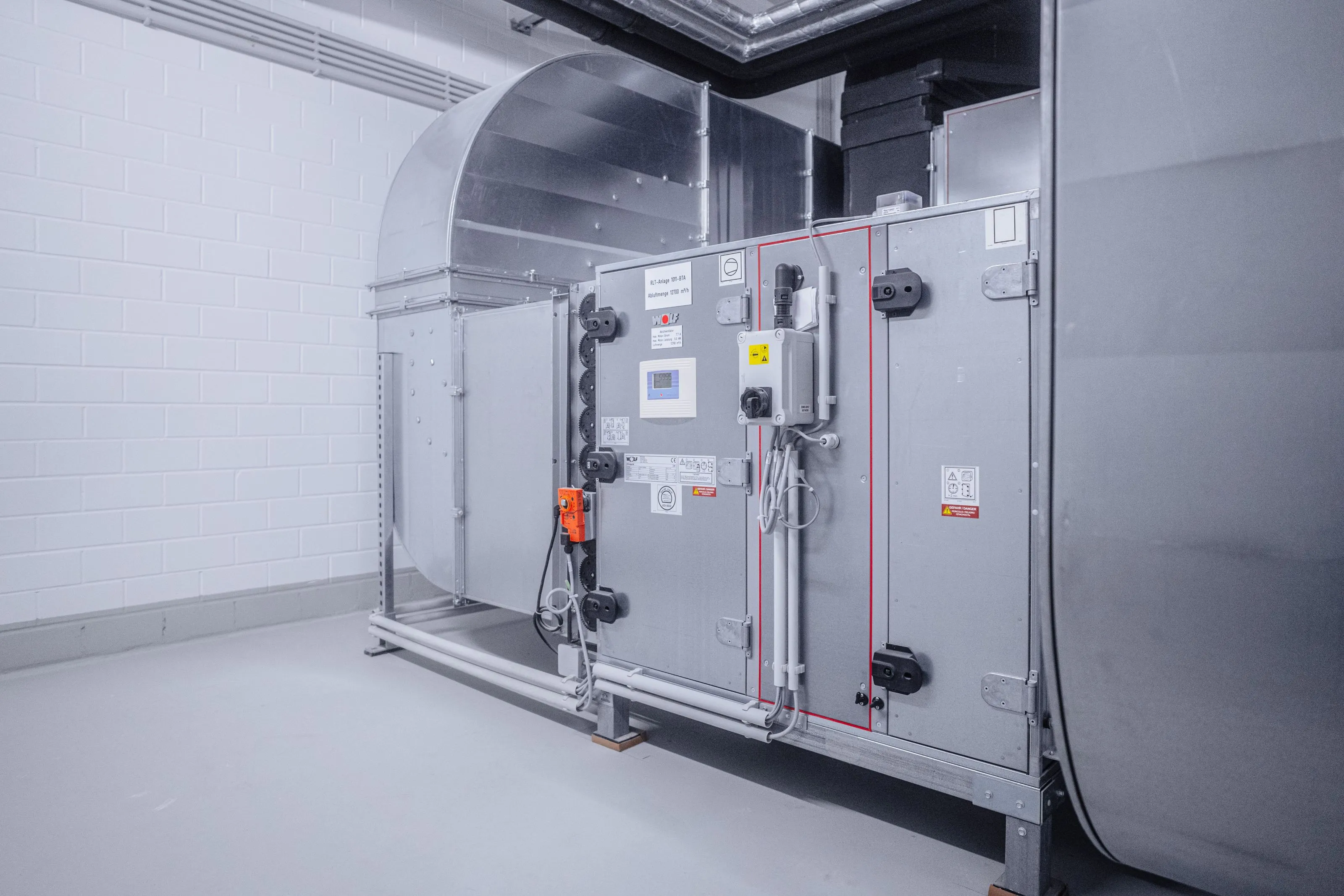 Industrielle Lüftungsanlage aus Metall in einem sauberen Raum mit weißen Fliesenwänden.