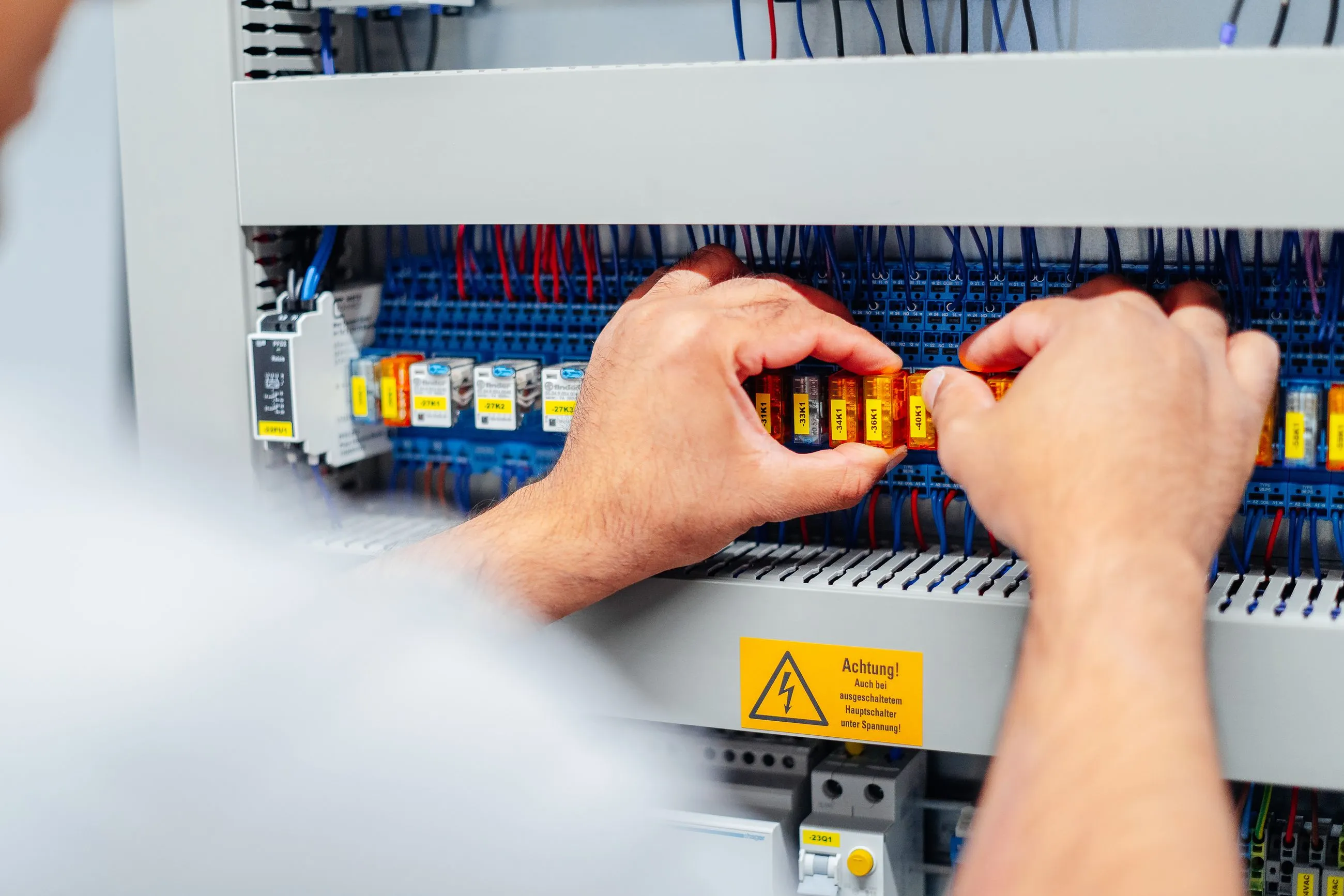 Hände eines Technikers, der in einem Schaltschrank eine orangefarbene Sicherung prüft oder installiert.