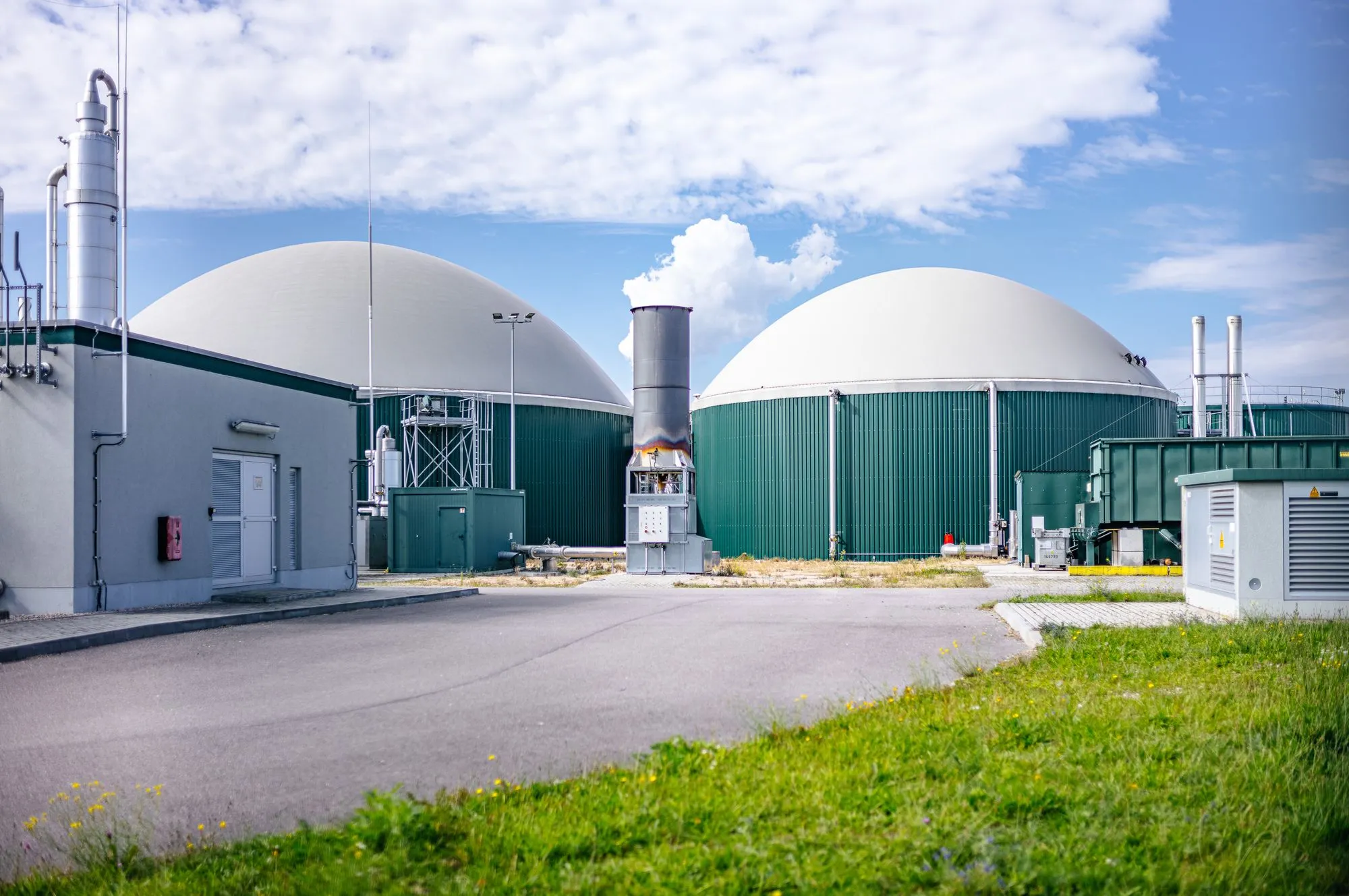 Industrieanlage mit zwei großen weißen Kuppelspeichern und umliegenden technischen Gebäuden unter blauem Himmel.