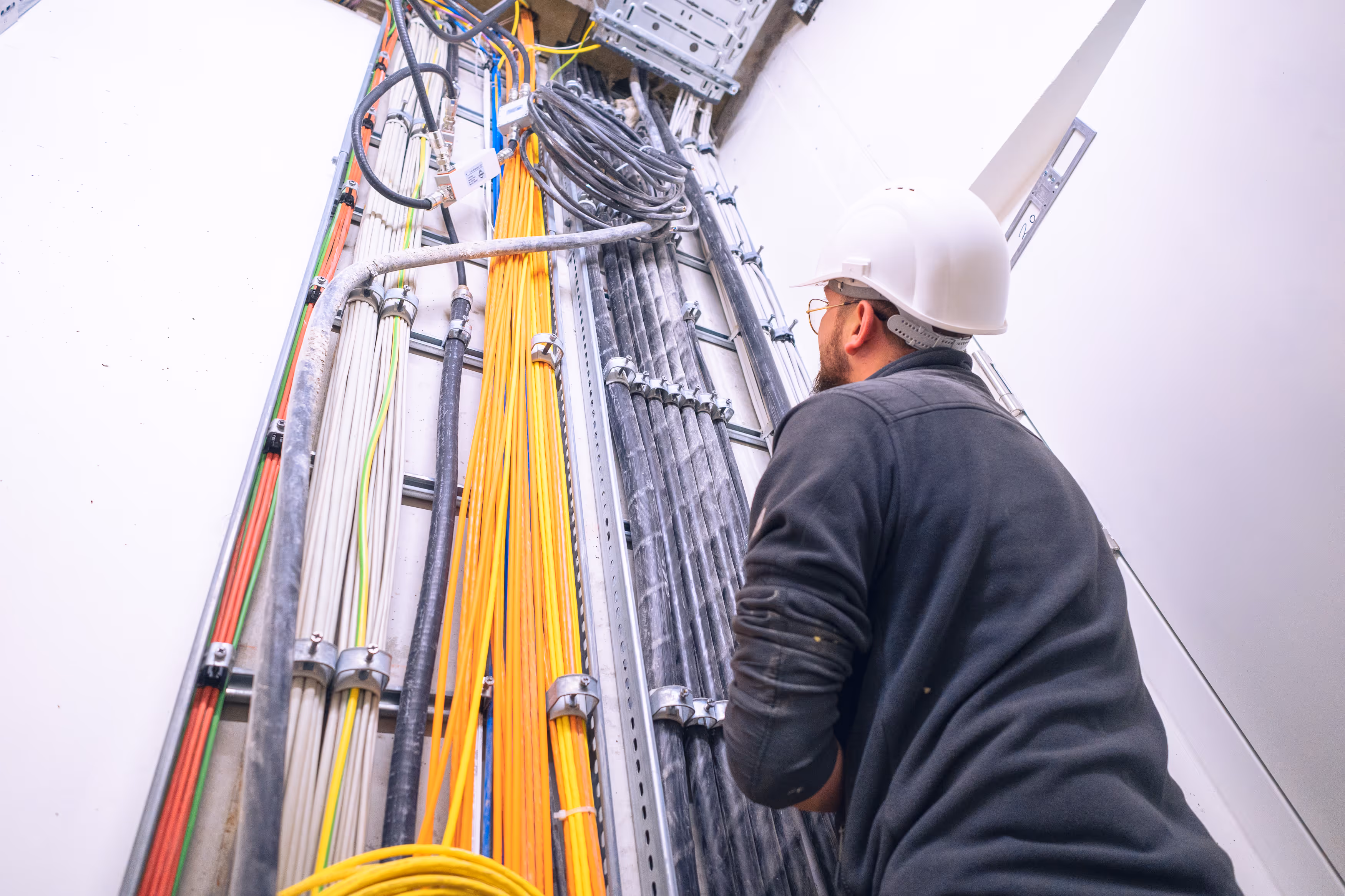 Elektriker mit Helm überprüft organisierte Kabelstränge an einer Wand in einem Gebäude.