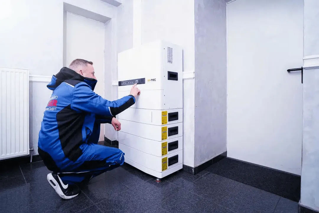 Techniker in blauer Arbeitskleidung bedient ein weißes Energiespeichersystem eines Photovoltaik-Systems in einem modernen Innenraum.