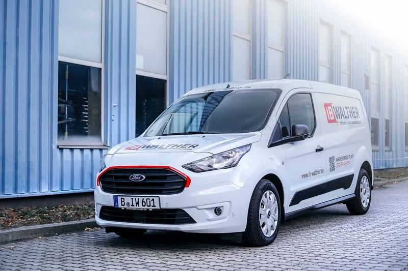 Weißer Ford Transporter mit IB Walther Firmenlogo und Werbetext, geparkt vor einem blauen Industriegebäude.