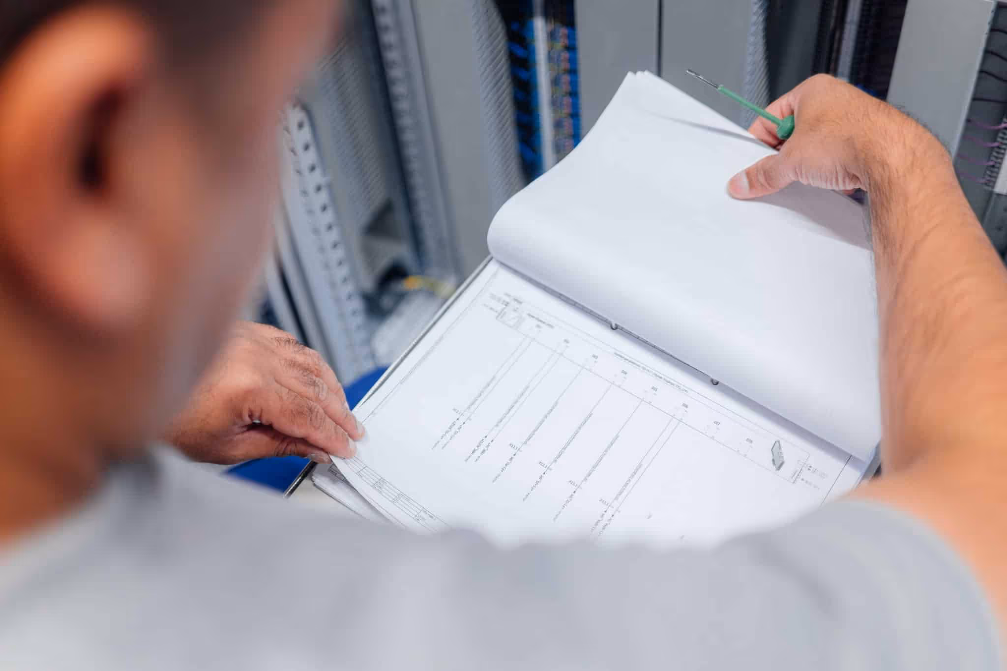 Techniker überprüft technische Zeichnungen oder Pläne in einem Ordner vor einem Schaltschrank.