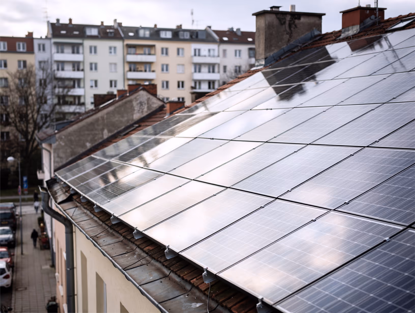 Solarmodule auf dem Schrägdach eines Gebäudes in einer städtischen Wohngegend mit Mehrfamilienhäusern im Hintergrund.