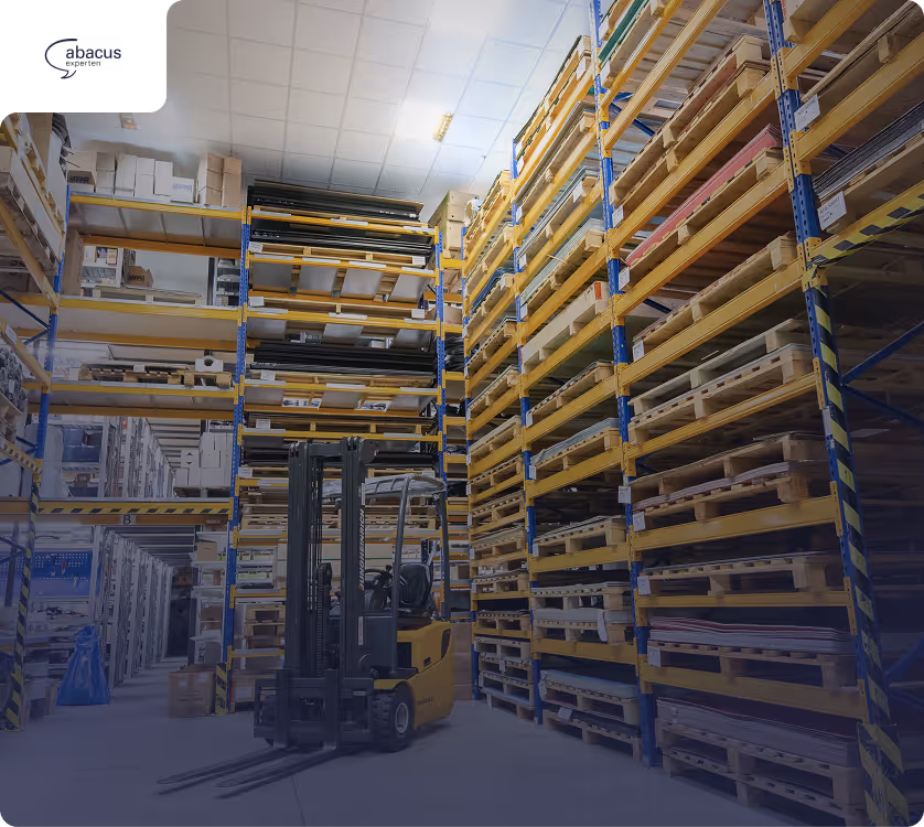 Innenansicht eines Lagers mit hohen Regalen voller Paletten und einem gelben Gabelstapler in der Mitte.